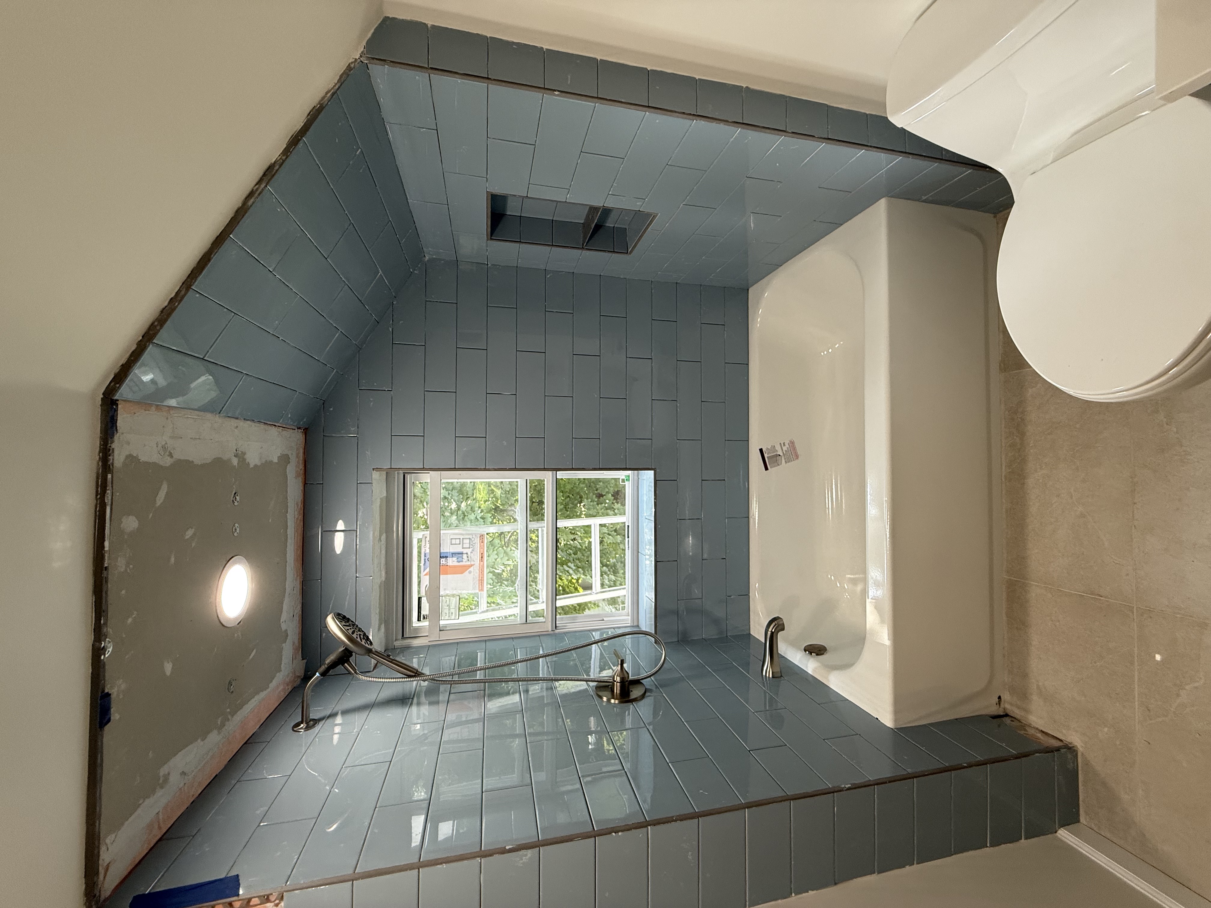 Bathroom featuring blue subway tile shower, white tub, and toilet after home renovation in [City], NJ.