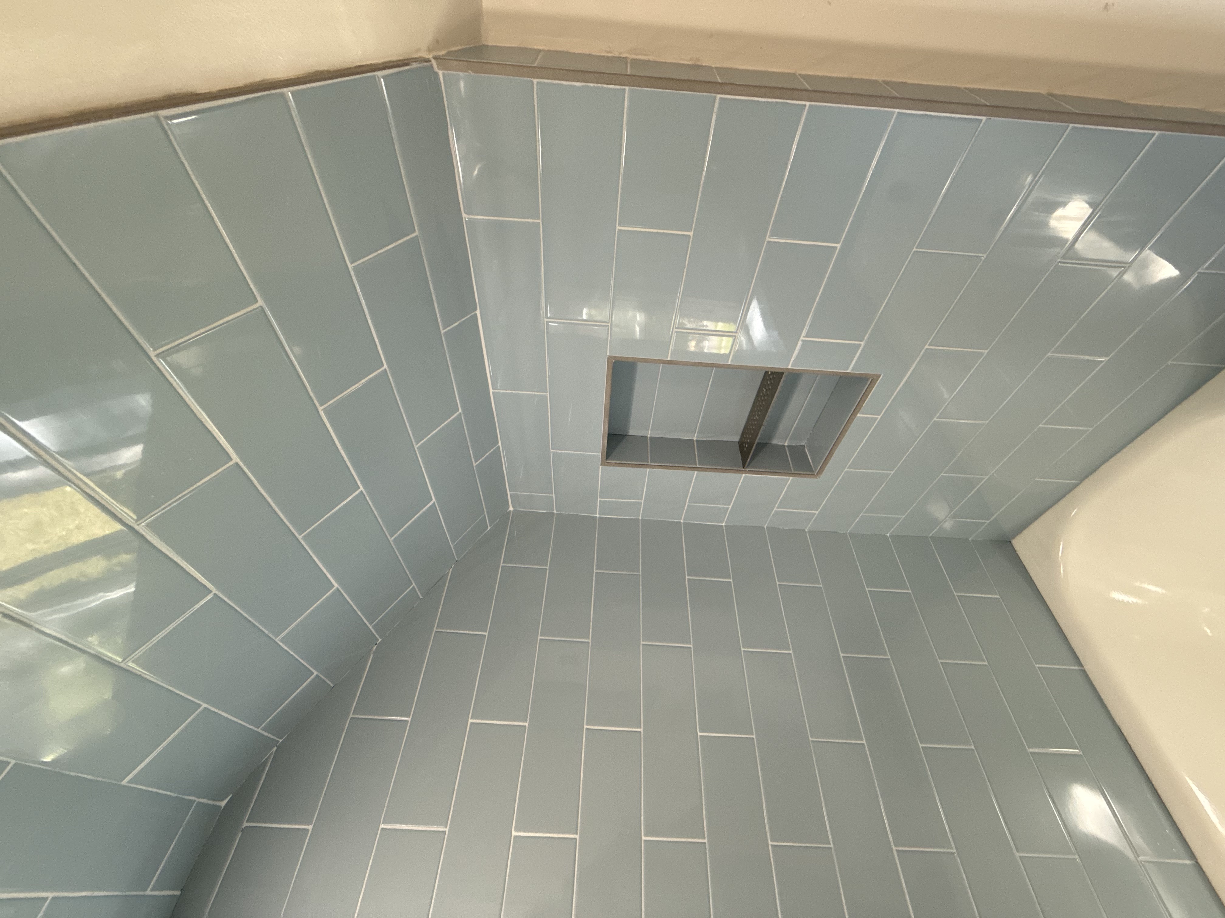 Bathtub surround with light blue subway tiles and recessed shower niche after bathroom remodeling in [City], NJ.