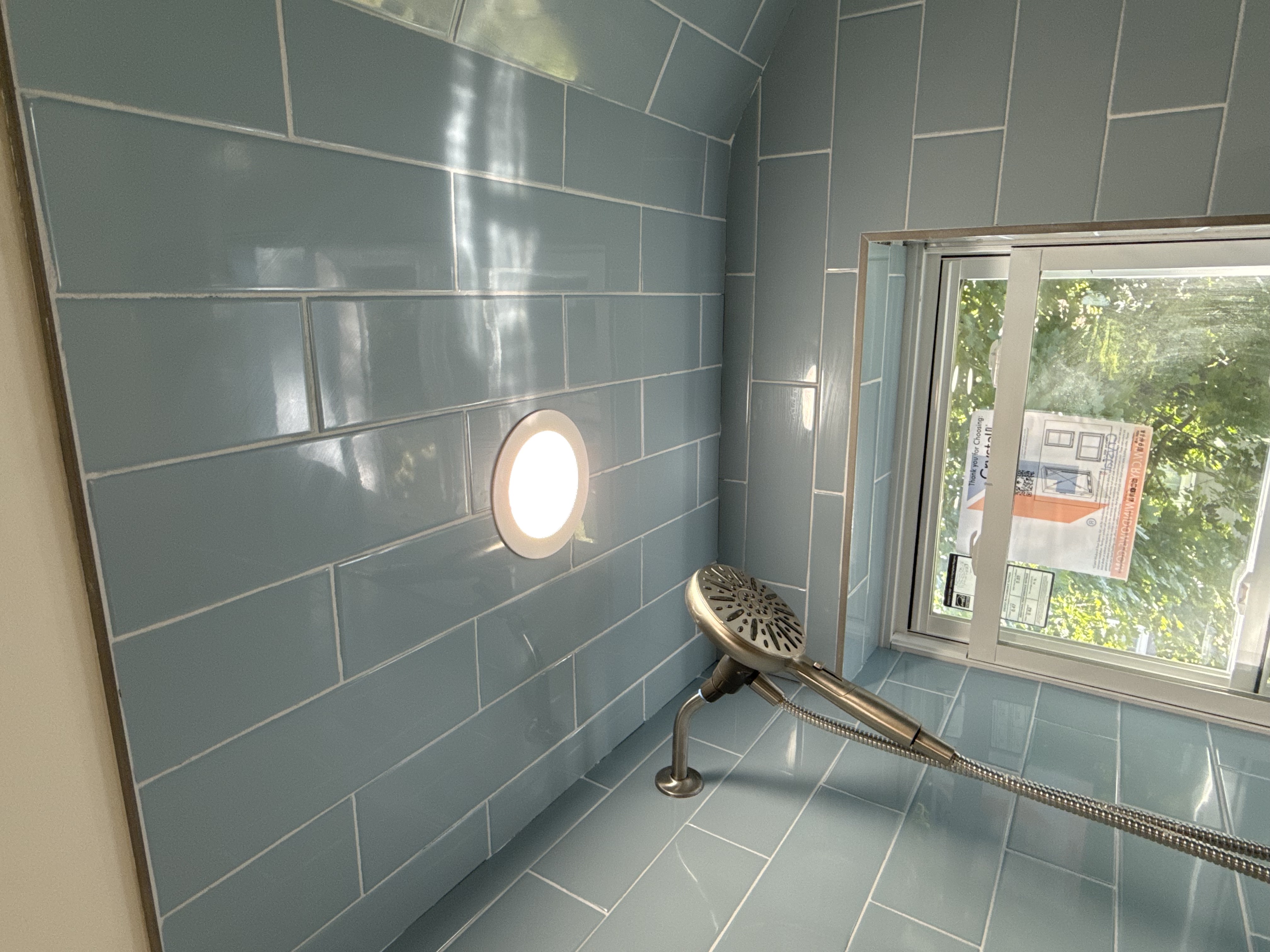 Bathroom shower with blue subway tiles, chrome shower head, recessed lighting, & new window after bathroom remodel in , NJ.