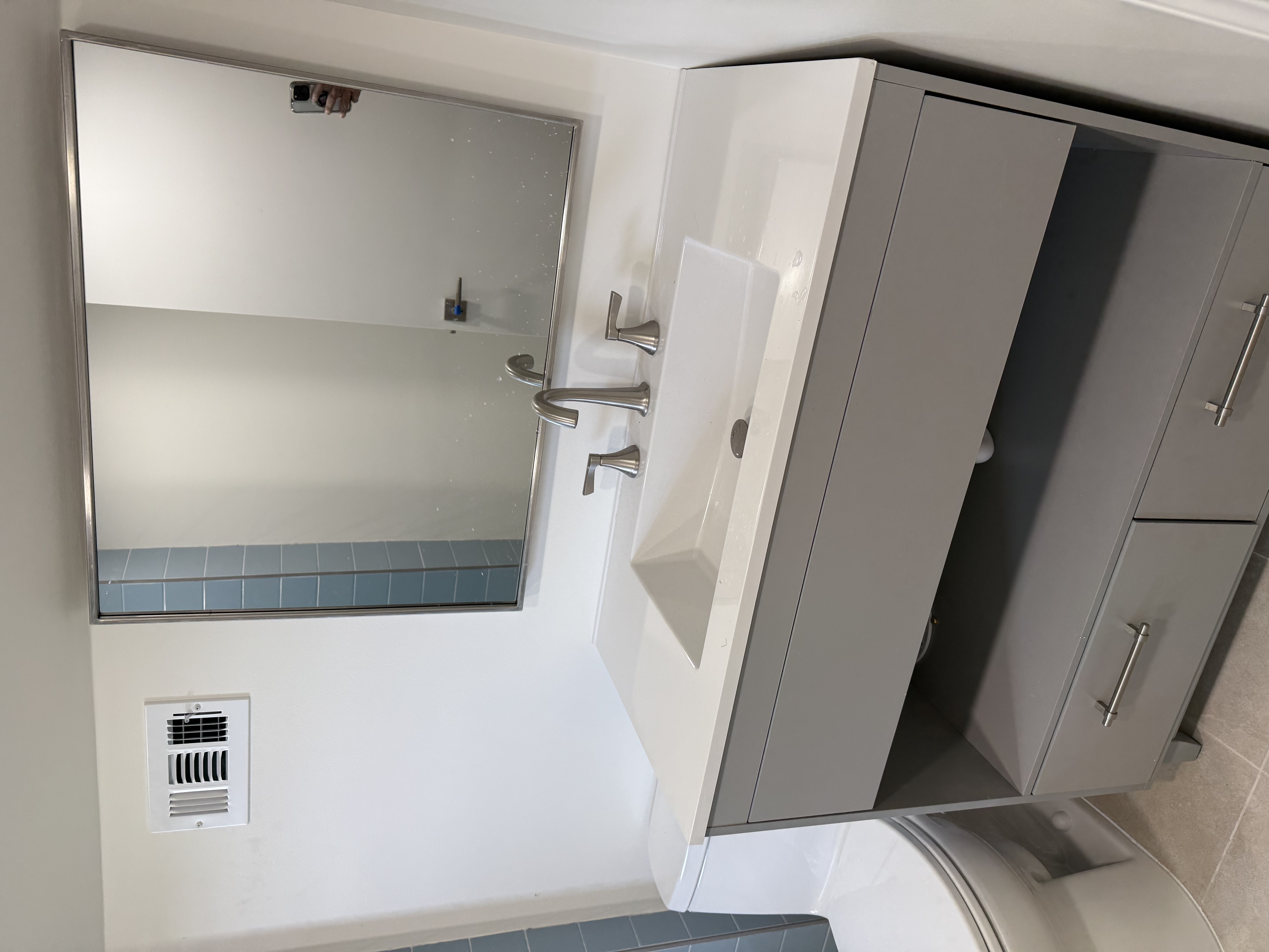 Bathroom featuring light gray vanity, white countertop, brushed nickel faucet, and framed mirror after bathroom remodeling in New Providence, NJ.