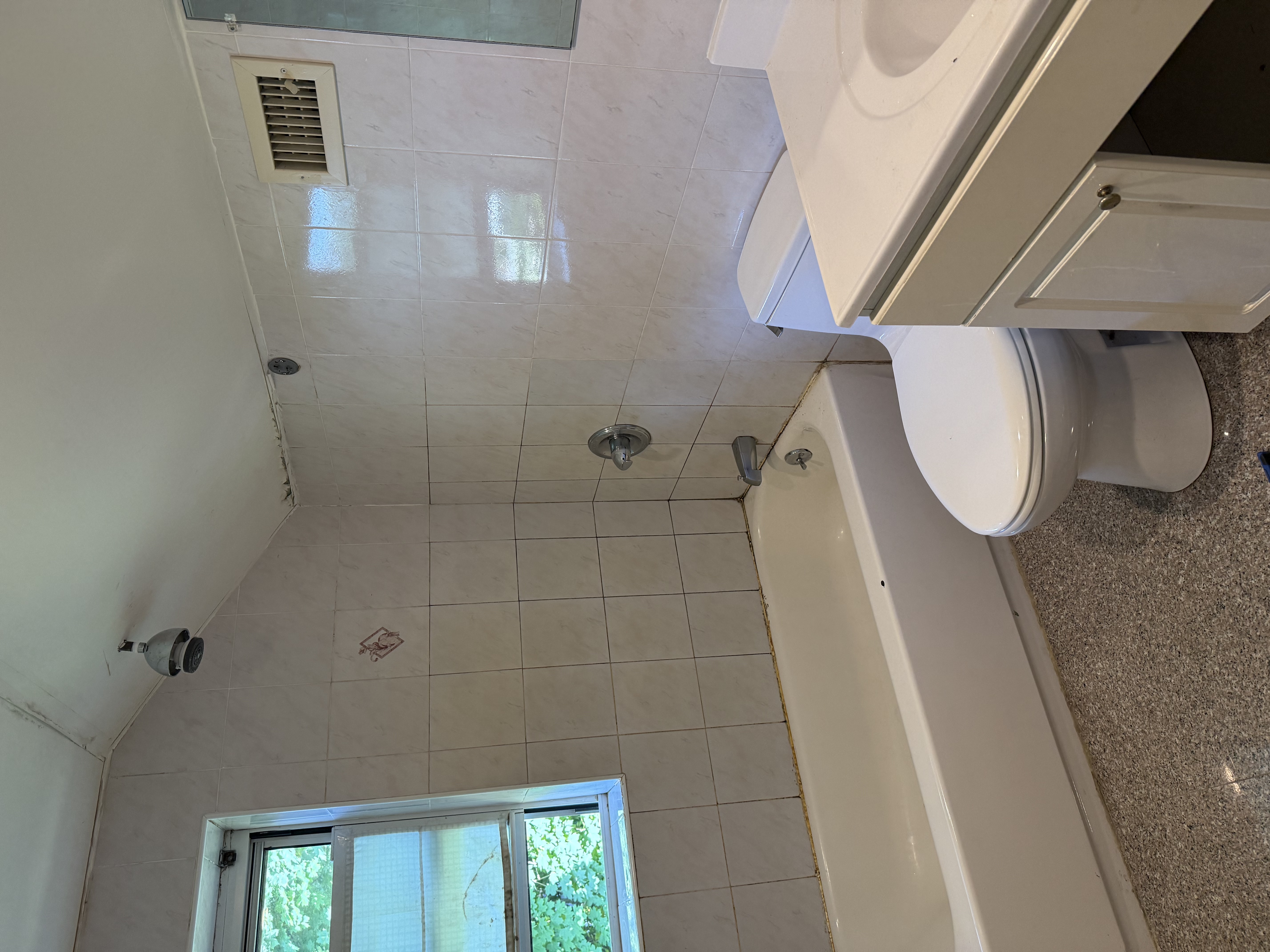 Dated bathroom with white ceramic wall tiles, speckled gray floor, and old fixtures before renovation in , NJ.
