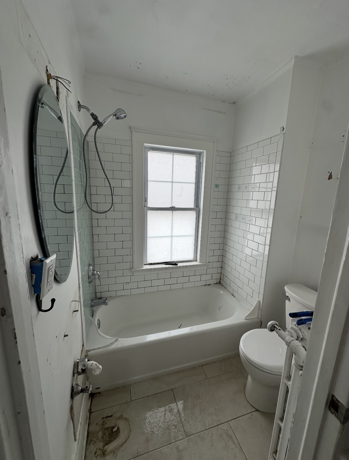 Dilapidated white tiled bathroom with bathtub, toilet, grimy floor tiles, and water damage on ceiling in Rahway, NJ.