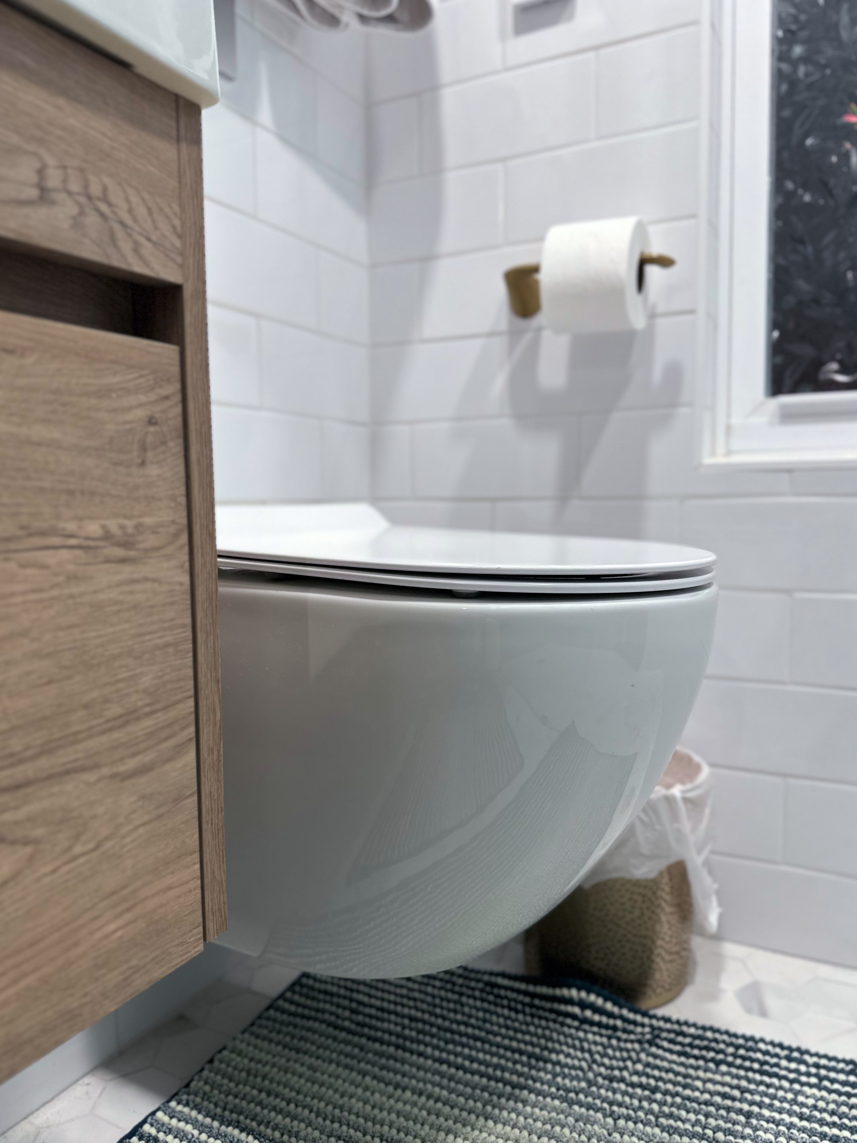 Bathroom featuring white subway tile walls, wood-look vanity, modern toilet, and hexagon floor tiles after Bathroom Renovation in Rahway, NJ.