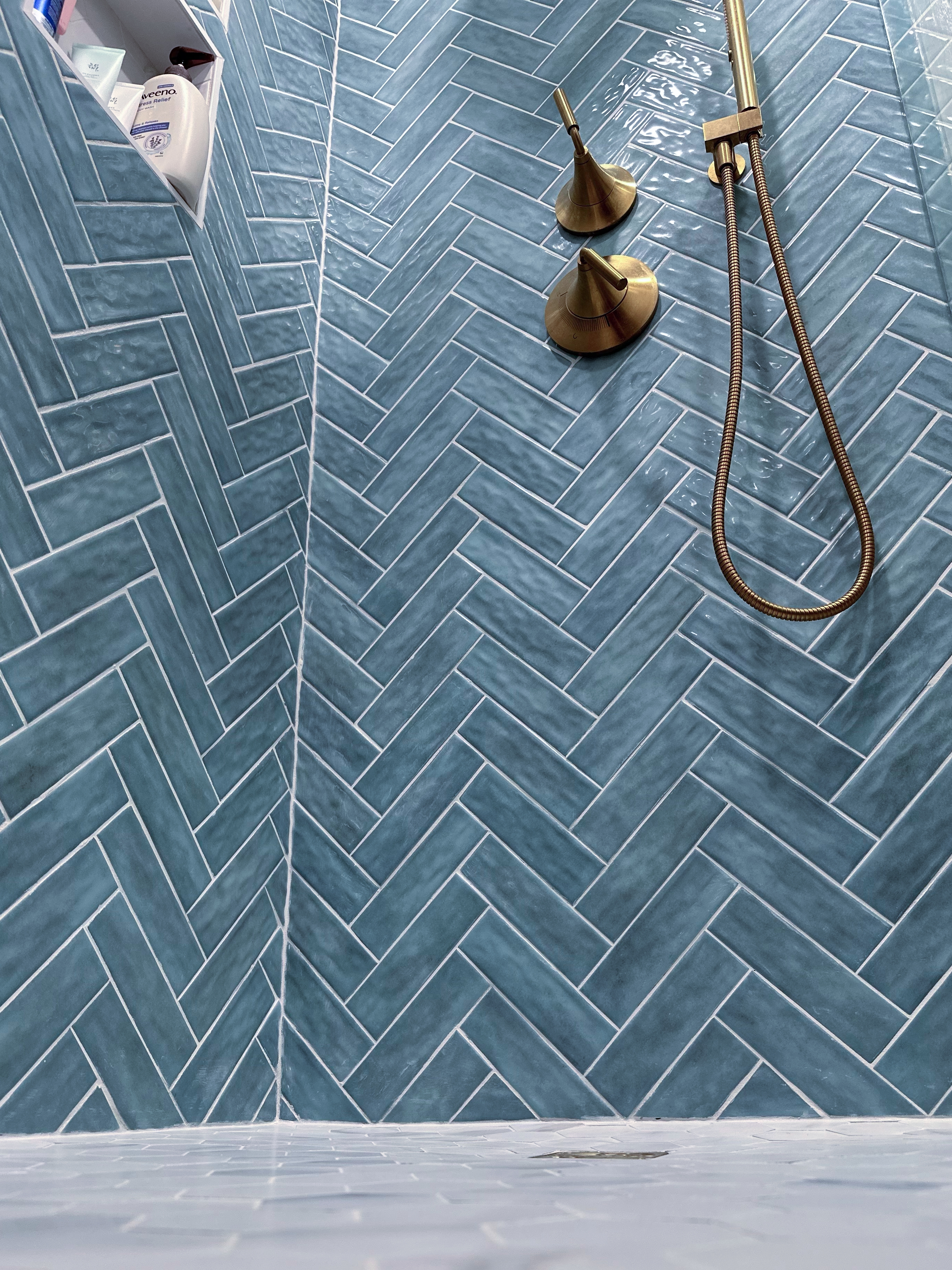Bathroom shower with blue herringbone subway tiles, polished brass fixtures, and a shower niche after Bathroom Renovation in Rahway, NJ.
