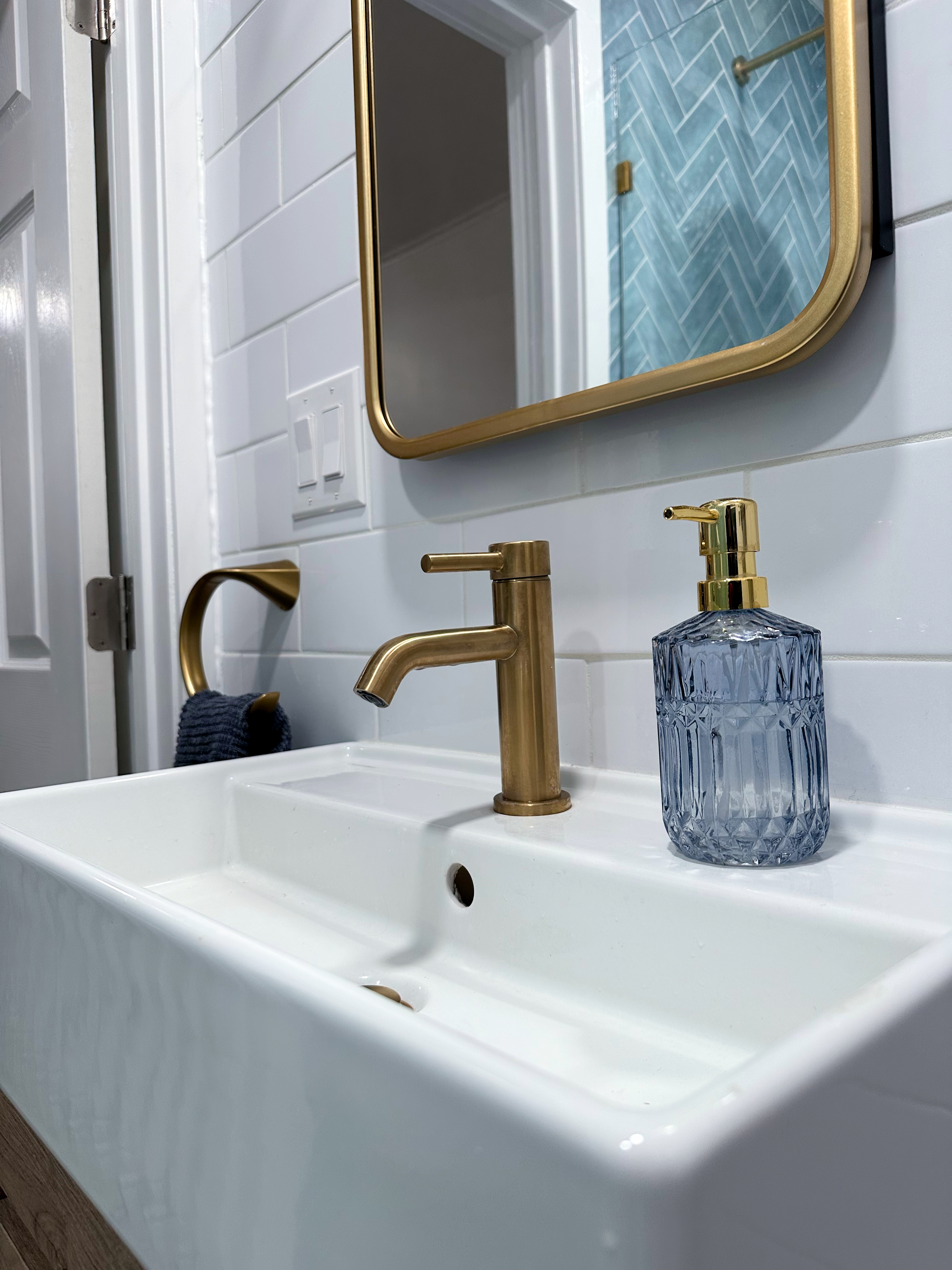 Modern bathroom featuring white subway tile, gold curved mirror, brass faucet, and white rectangular sink after Bathroom Renovation in Rahway, NJ.