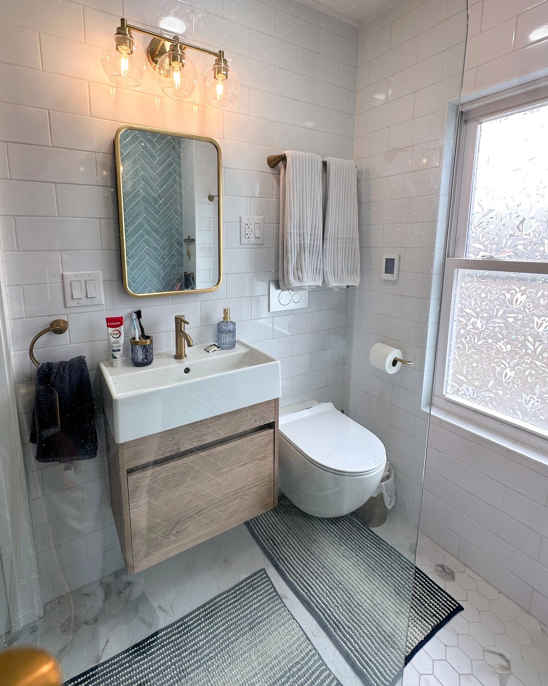 Bathroom featuring white subway tile walls, wood-look vanity, gold fixtures, and hexagon floor tiles after Bathroom Renovation in Rahway, NJ.