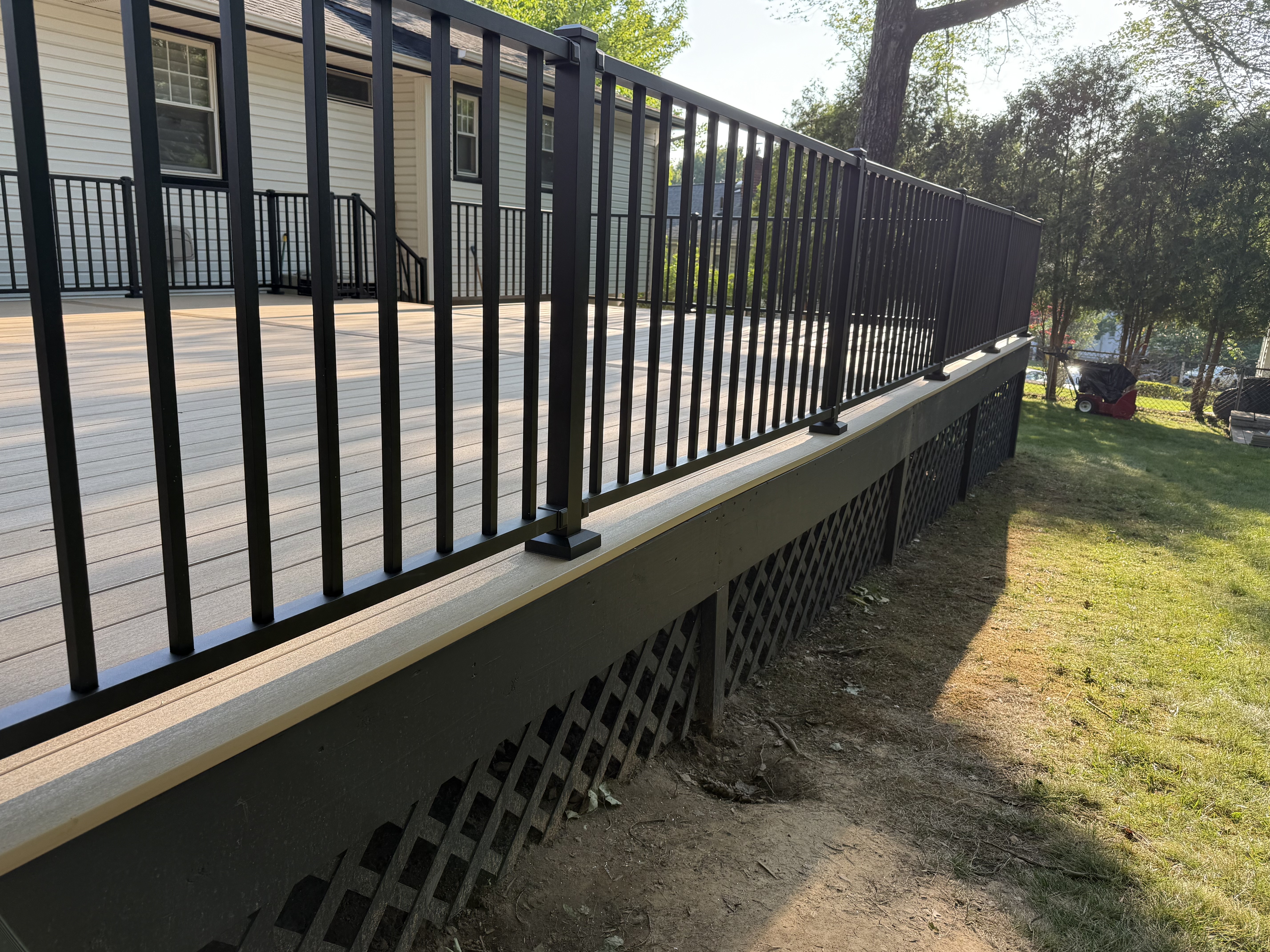 Outdoor deck renovation with composite decking, black aluminum railings, and lattice skirting in Cedar Grove, NJ.