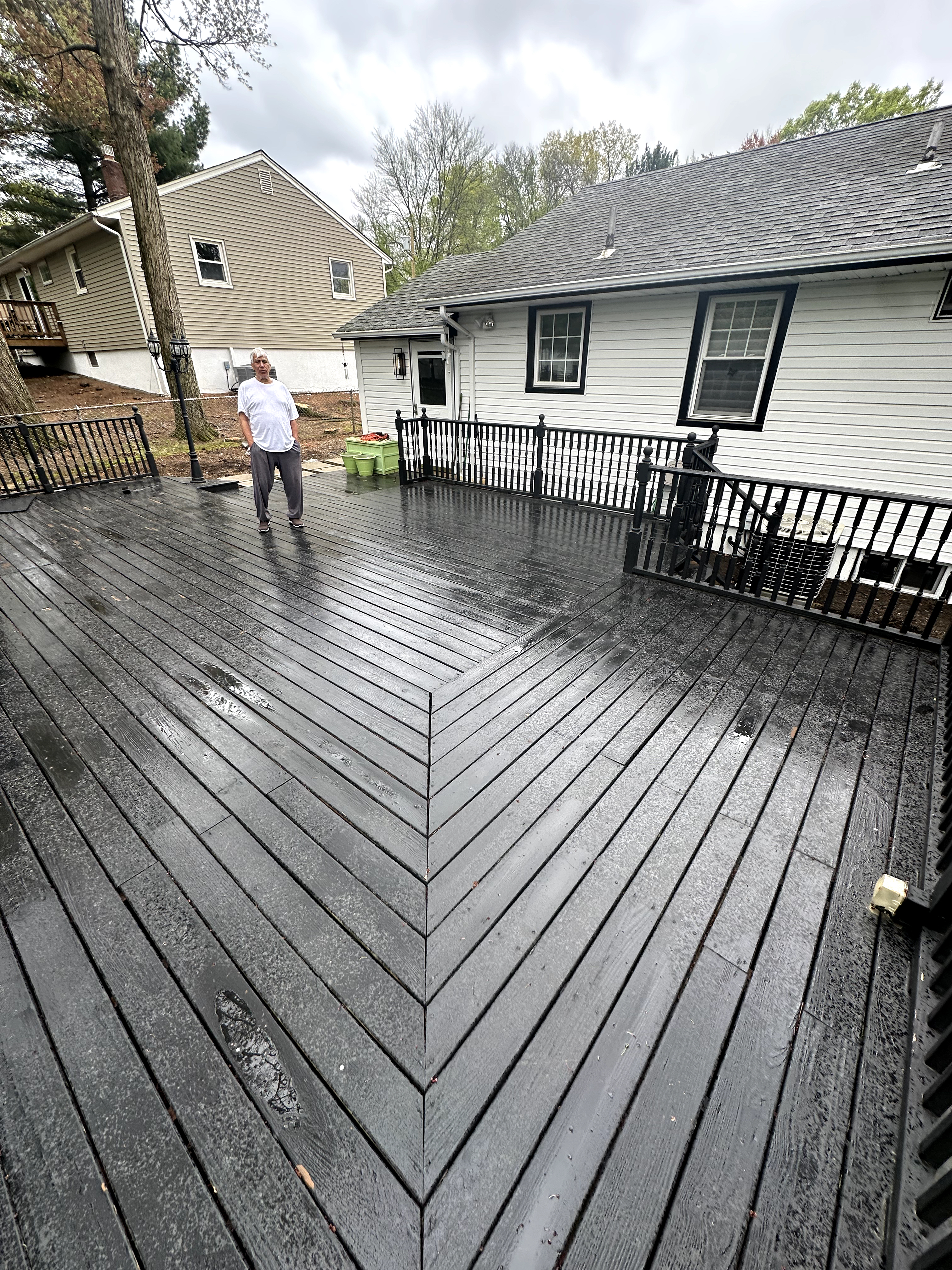 Exterior deck with faded black wood planks and dark railings in Cedar Grove, NJ, NJ before renovation, showing wear and water residue.
