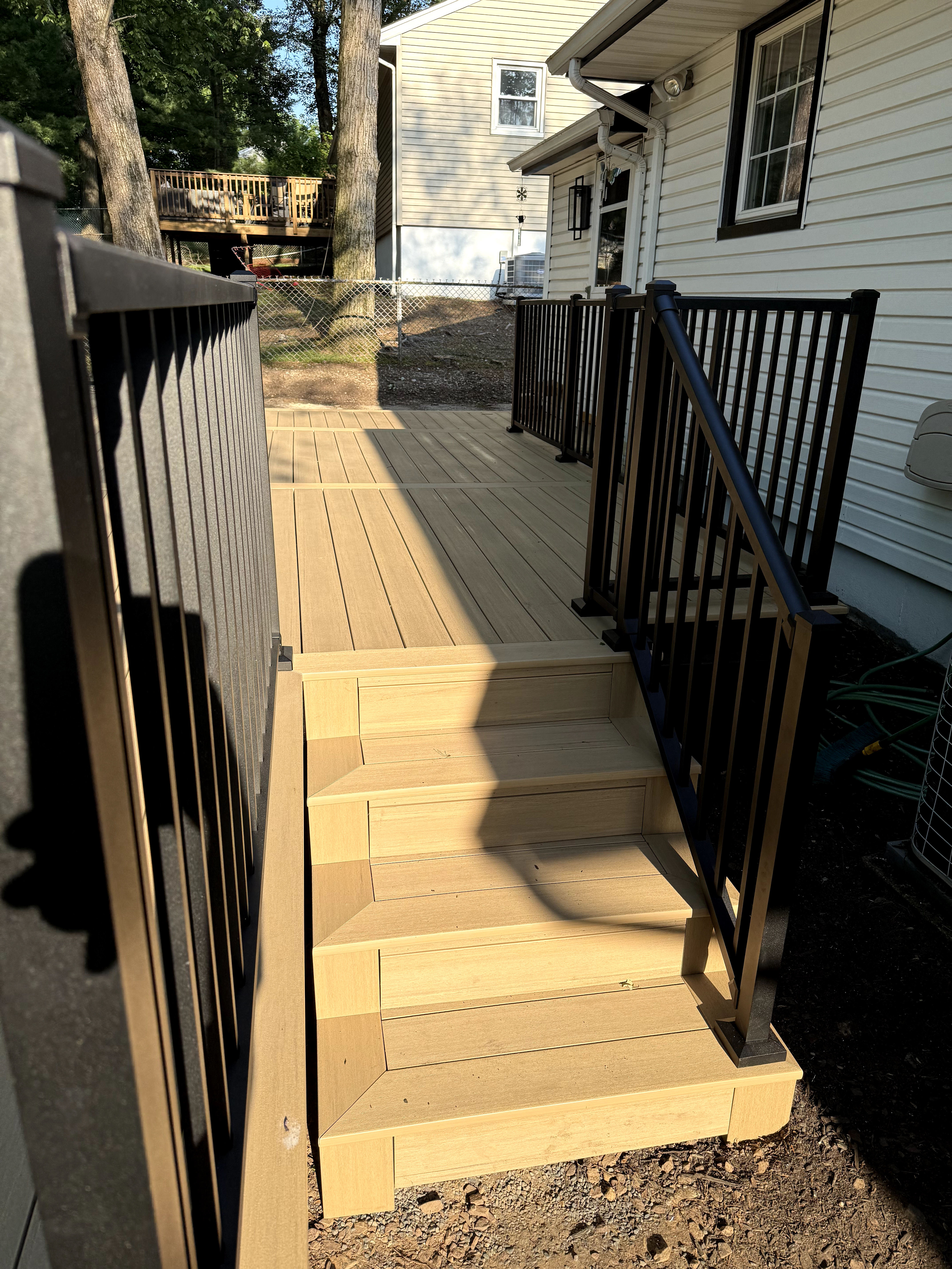 Deck with blonde composite decking and black railings, multistep staircase in Cedar Grove, NJ.