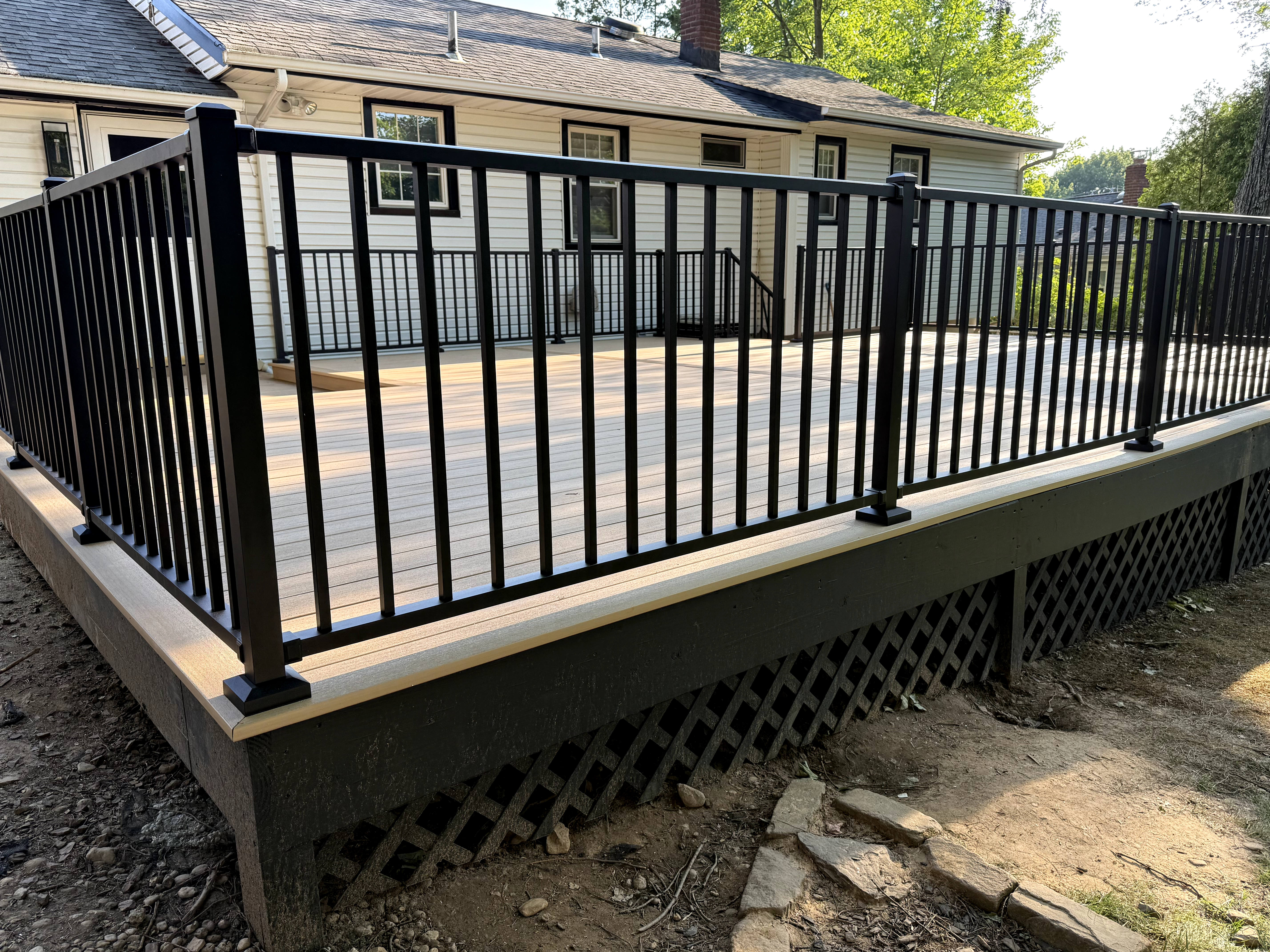 Renewed outdoor deck featuring light composite planks, black aluminum railings, and lattice work skirting in Cedar Grove, NJ, NJ.