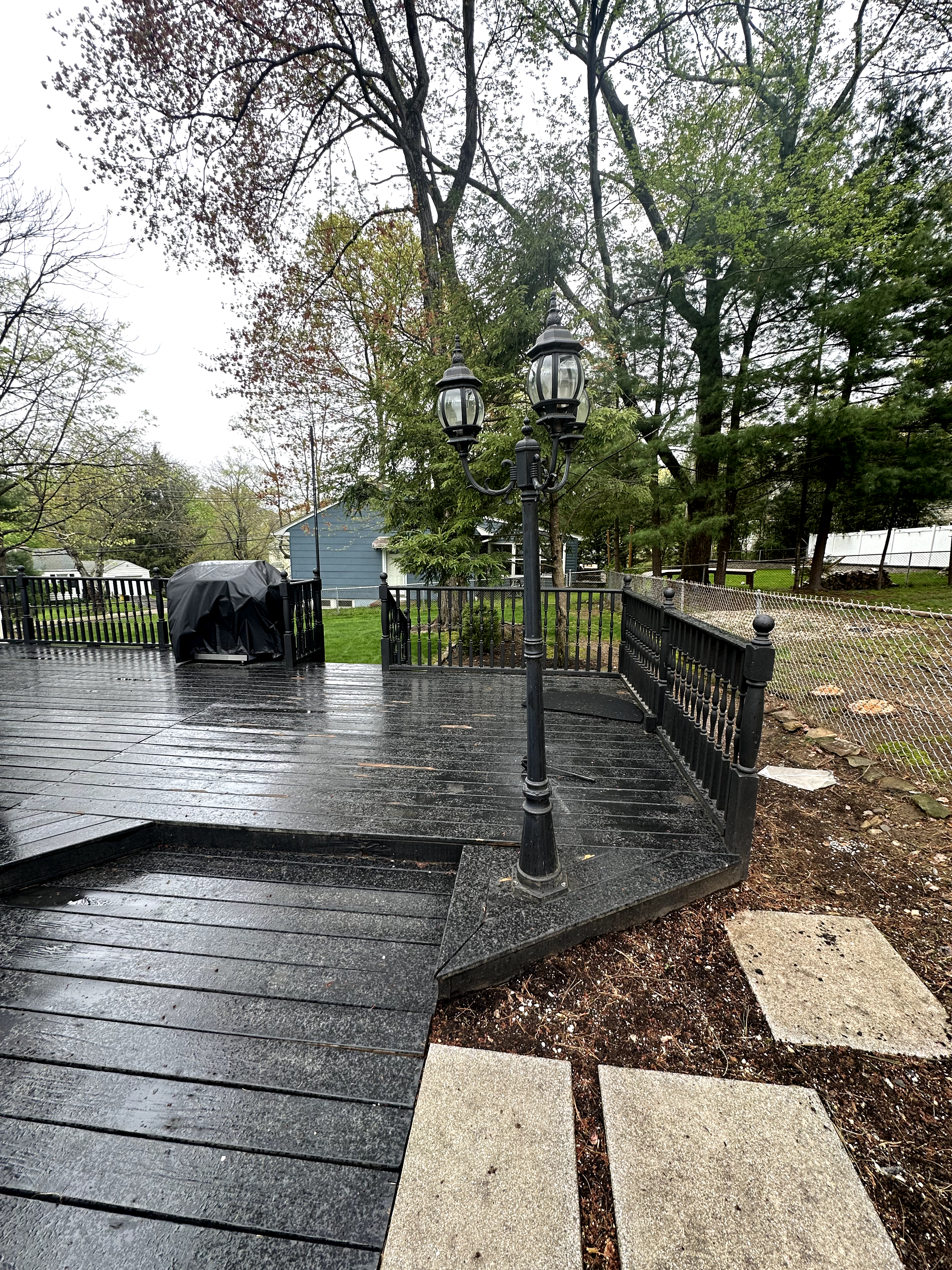 Exterior deck with weathered black wood planking, matching railings, and a lamp post in Cedar Grove, NJ, showing wear and peeling paint.