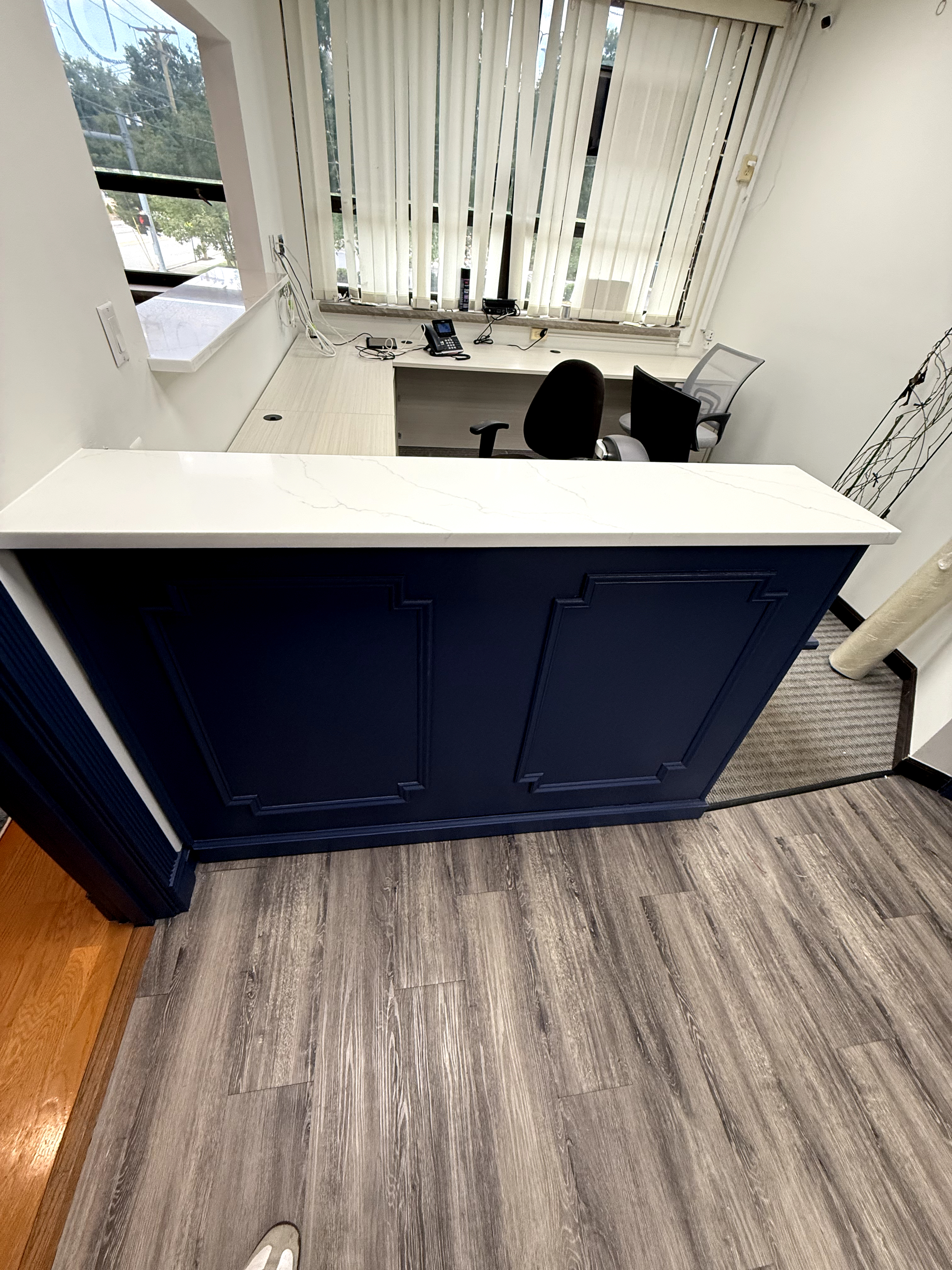 Office reception area with navy blue paneled front desk, white quartz counter, and grey wood-look flooring after Custom Office Space in Rochelle Park, NJ.