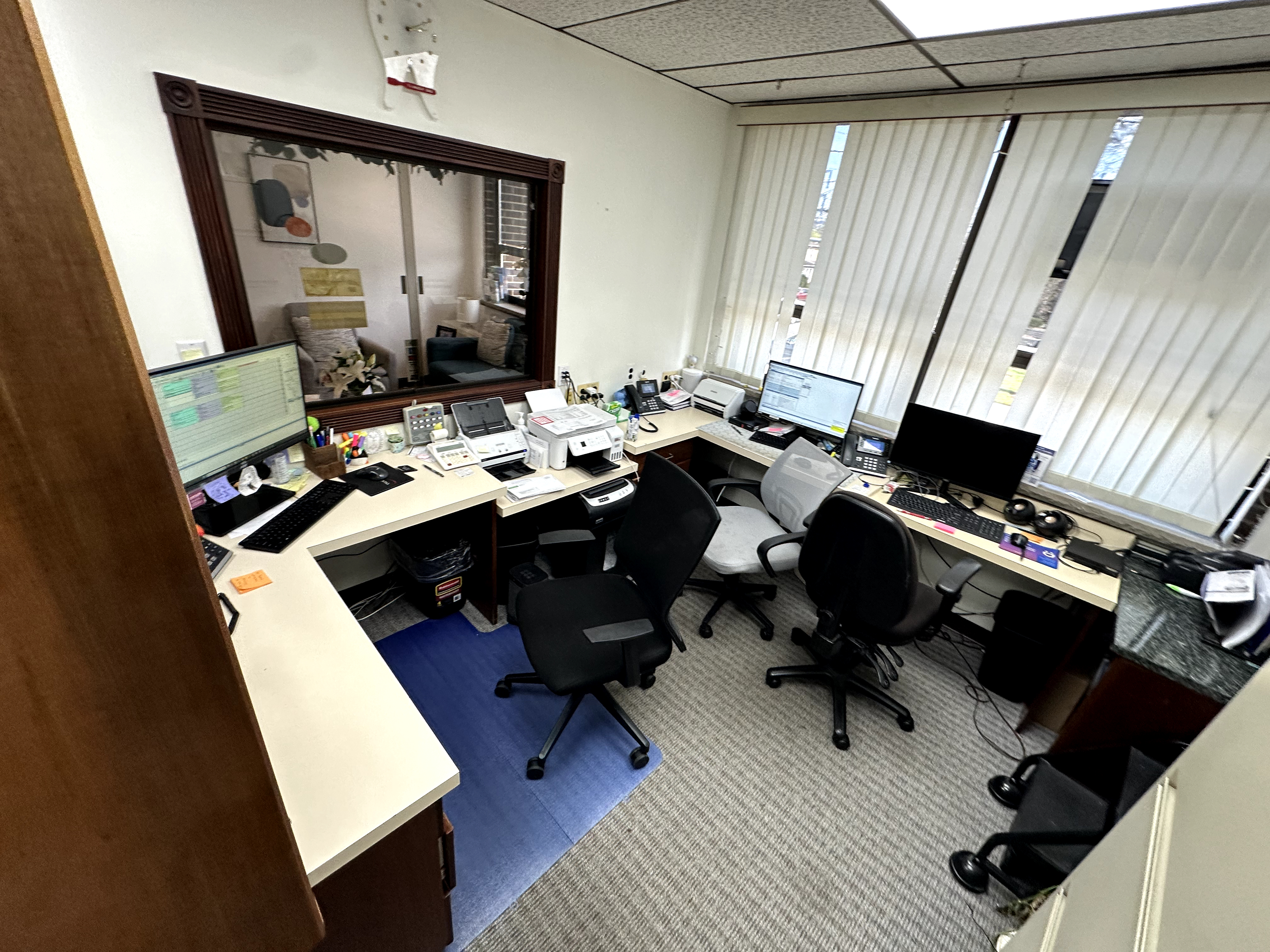 Office space with drop ceiling, striped gray carpet, white walls, and outdated beige composite countertops in Rochelle Park, NJ.