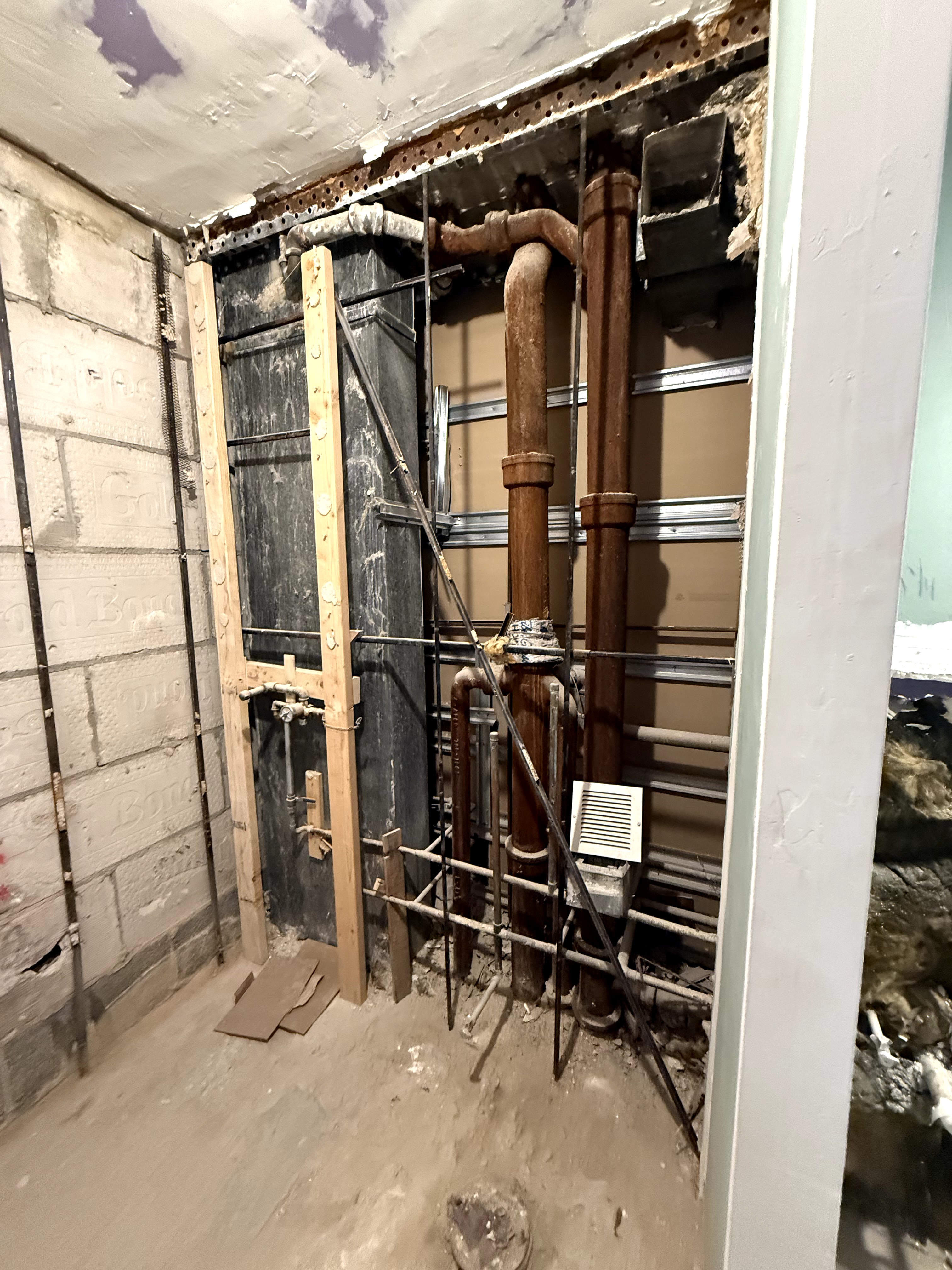 Bathroom pre-renovation showing exposed plumbing and unfinished walls