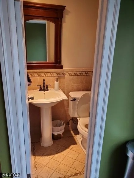 Powder room with outdated pedestal sink, tiled floors/walls, wooden mirror, and light green paint in West Orange, NJ before renovation.