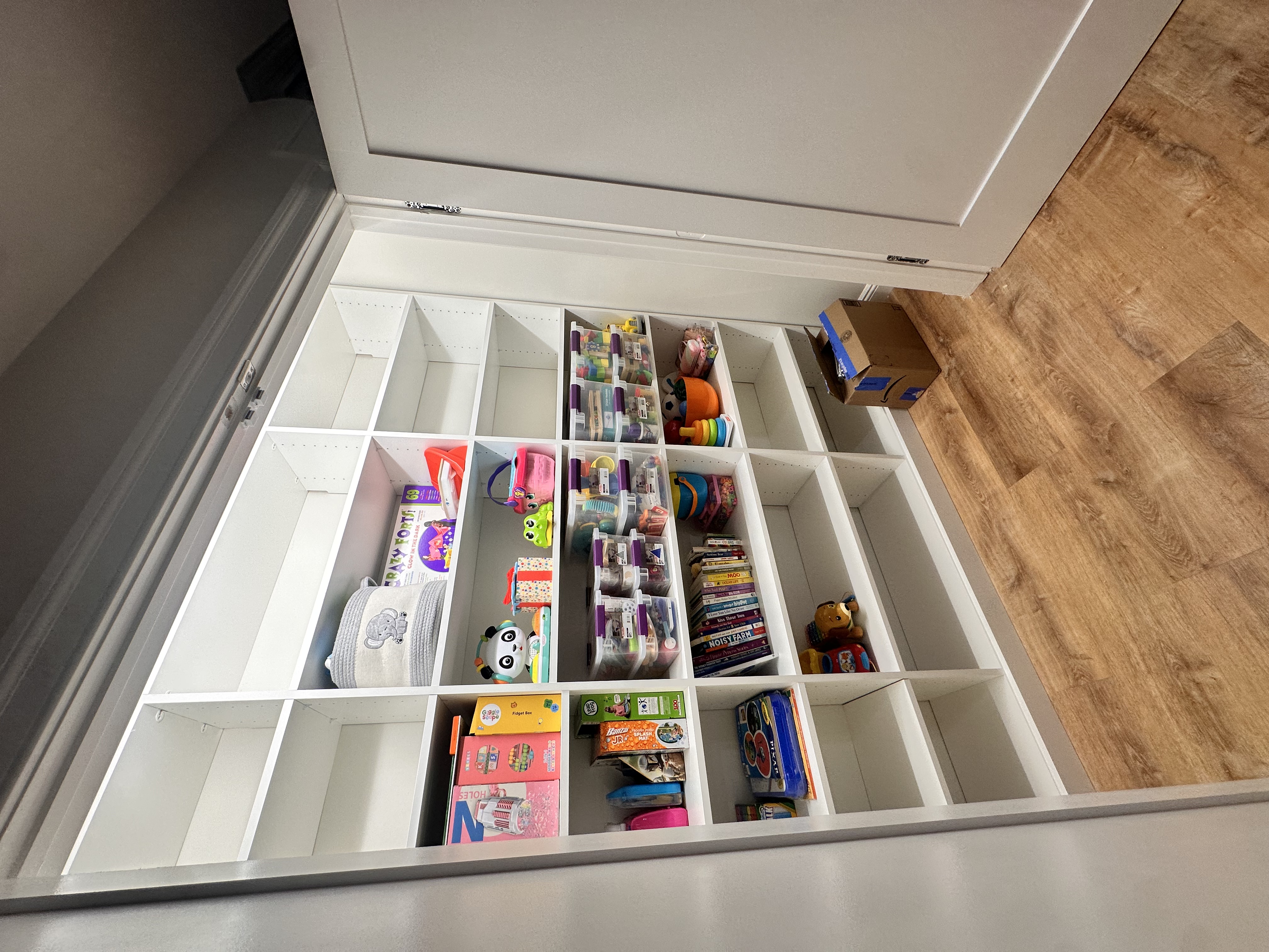 Basement playroom with white built-in shelving, organized toys, and light wood-look flooring after Basement Finishing in Kinnelon, NJ.