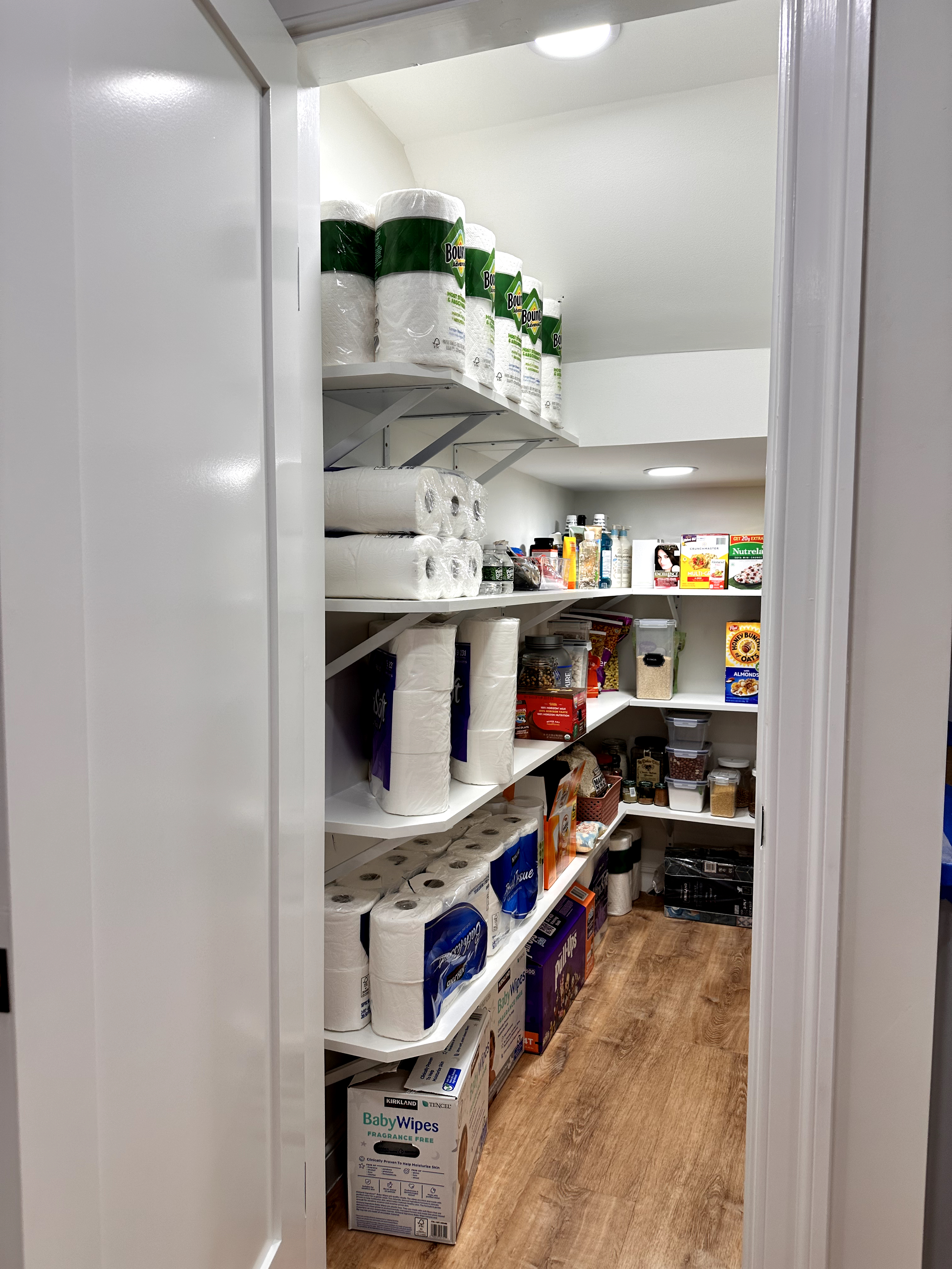 Pantry closet featuring white adjustable shelving, recessed lighting, and wood-look laminate flooring after Basement Finishing in Kinnelon, NJ.