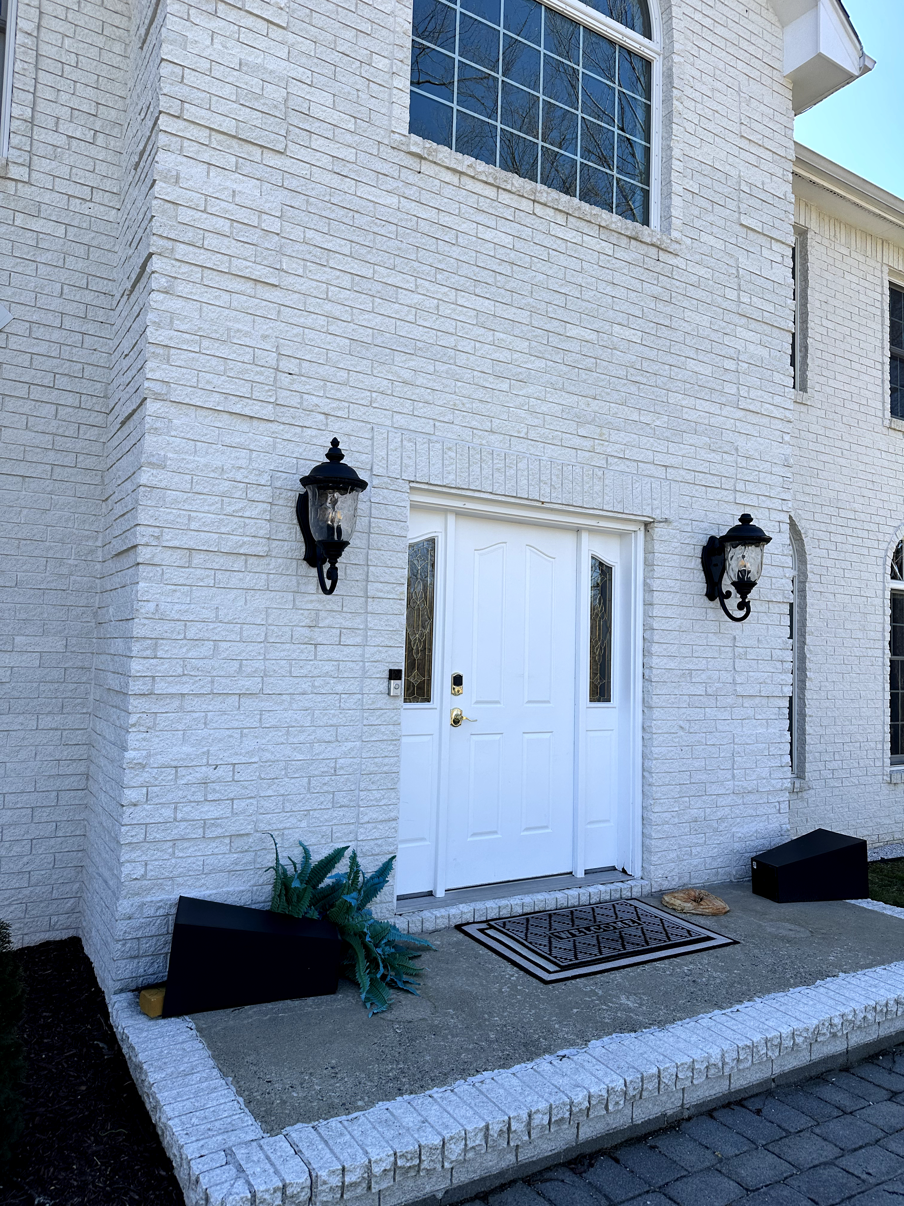 Exterior of white painted brick house with arched windows, black lanterns, and concrete steps in Kinnelon, NJ before renovation.