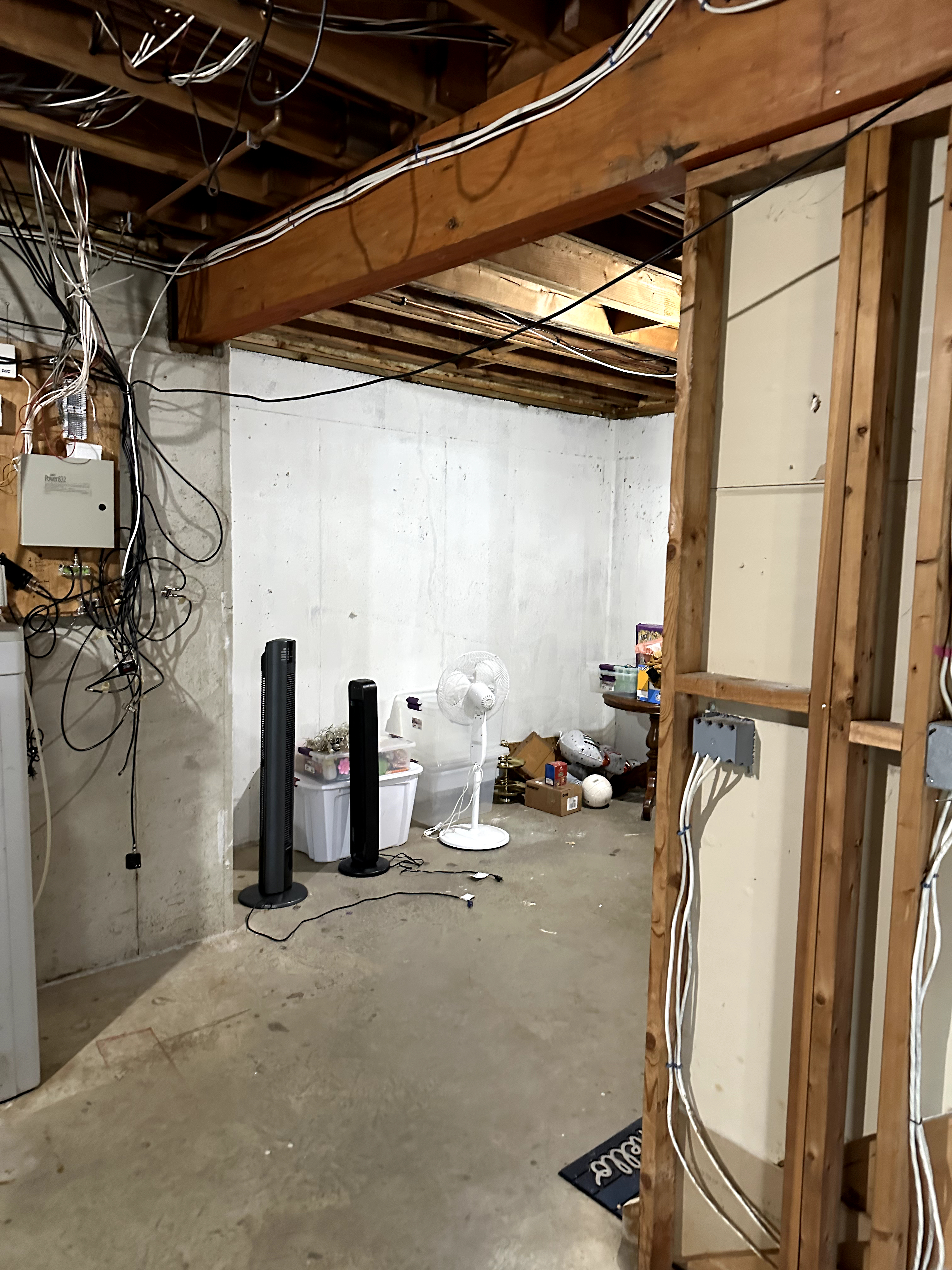 Unfinished basement with concrete floor, exposed wood beams, white cinder block walls, and visible wiring in Kinnelon, NJ before renovation.