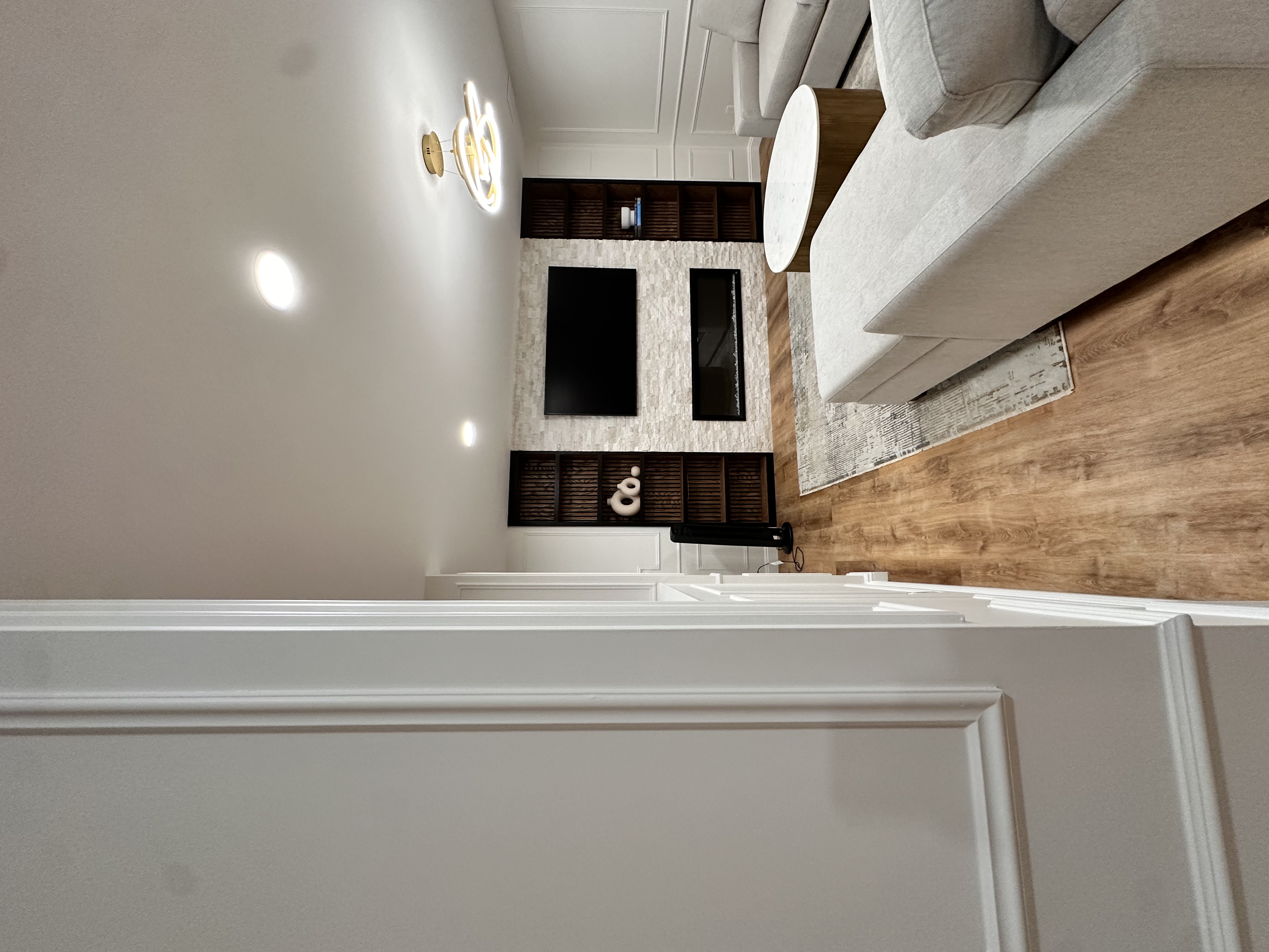 Basement living room with wood-look flooring, light gray sofas, and a marble & wood coffee table after Basement Finishing in Kinnelon, NJ