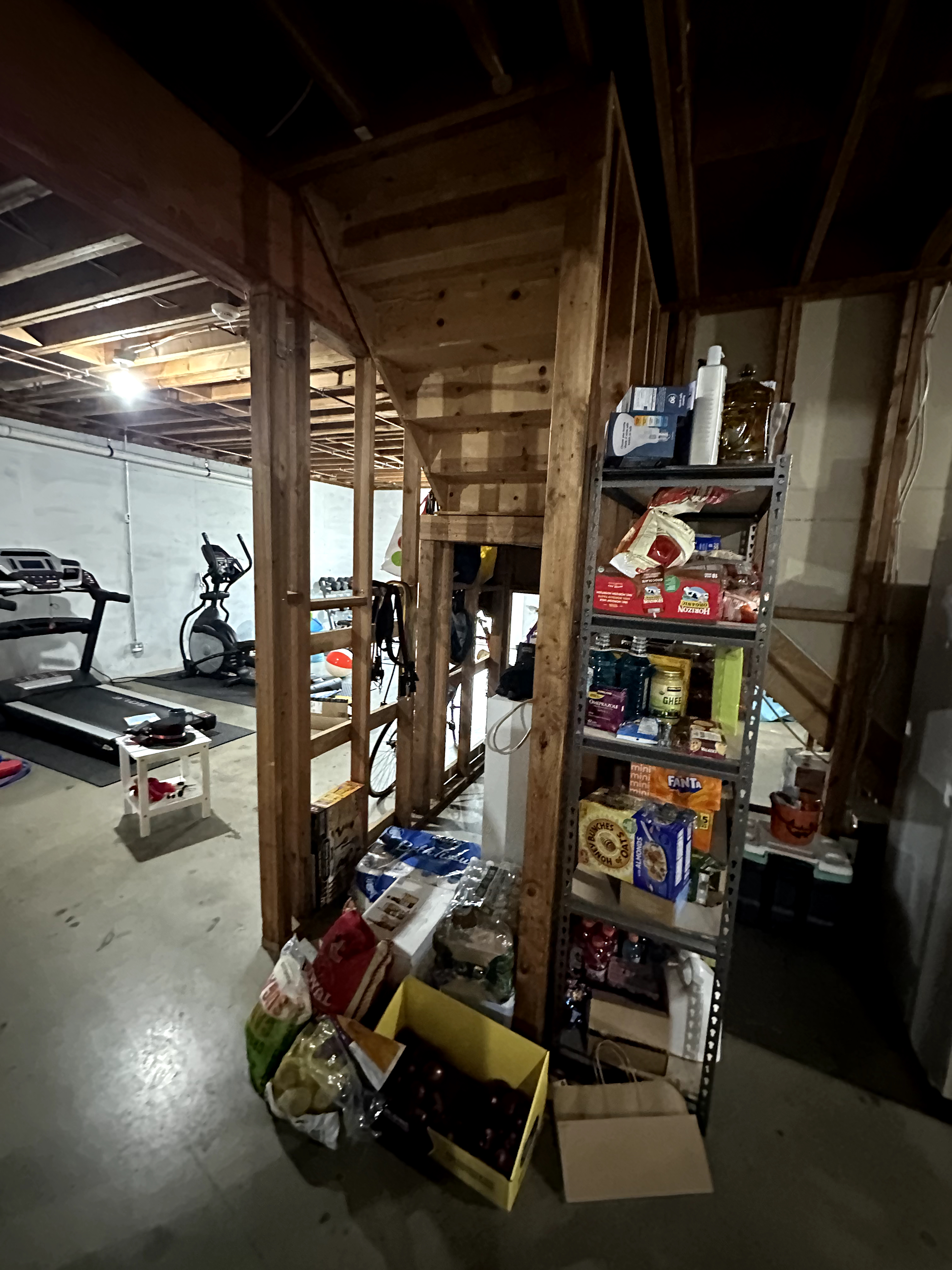 Kinnelon, NJ unfinished basement before renovation with exposed wood framing, concrete floor, white block walls, and cluttered storage areas.
