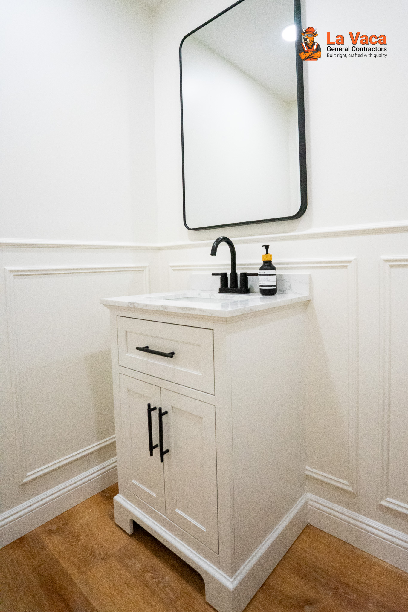 Bathroom vanity with white shaker cabinets, marble countertop, black fixtures, and wainscoting after Basement Finishing in Kinnelon, NJ
