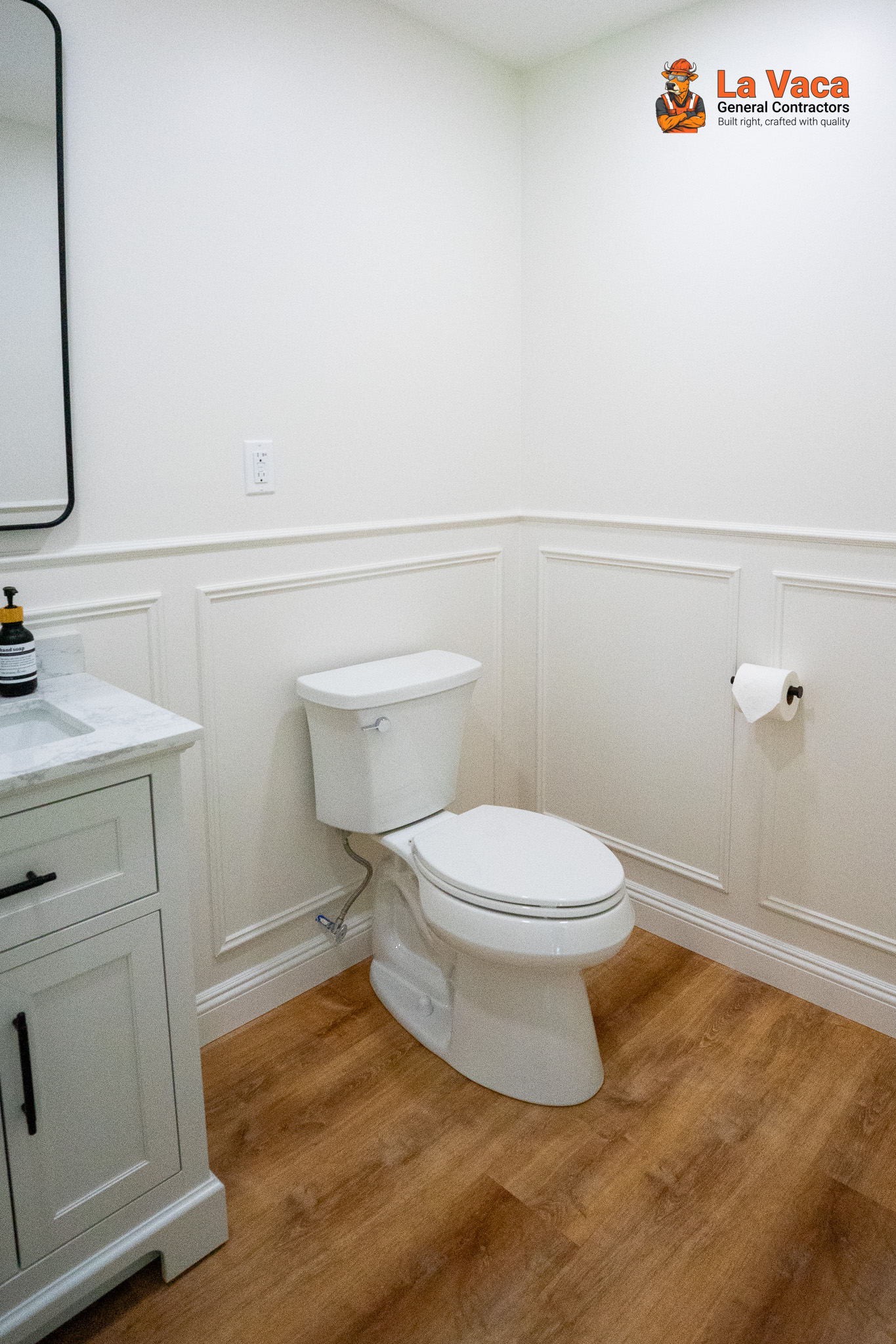 Basement bathroom featuring white wainscoting, toilet, vanity with marble top, and wood-look flooring after Basement Finishing in Kinnelon, NJ