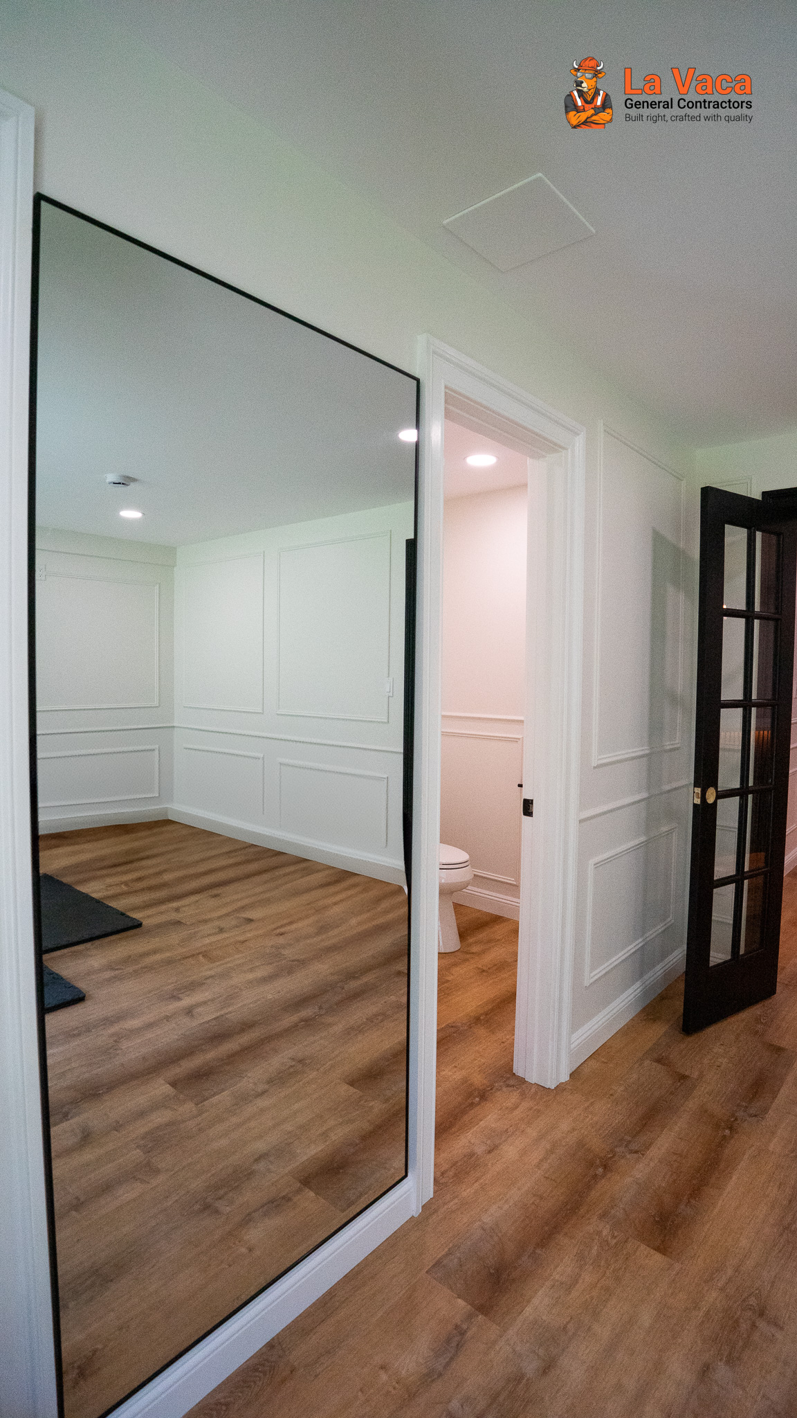 Finished basement hallway with wood-look flooring, white paneling, and black-framed mirrors after Basement Finishing in Kinnelon, NJ