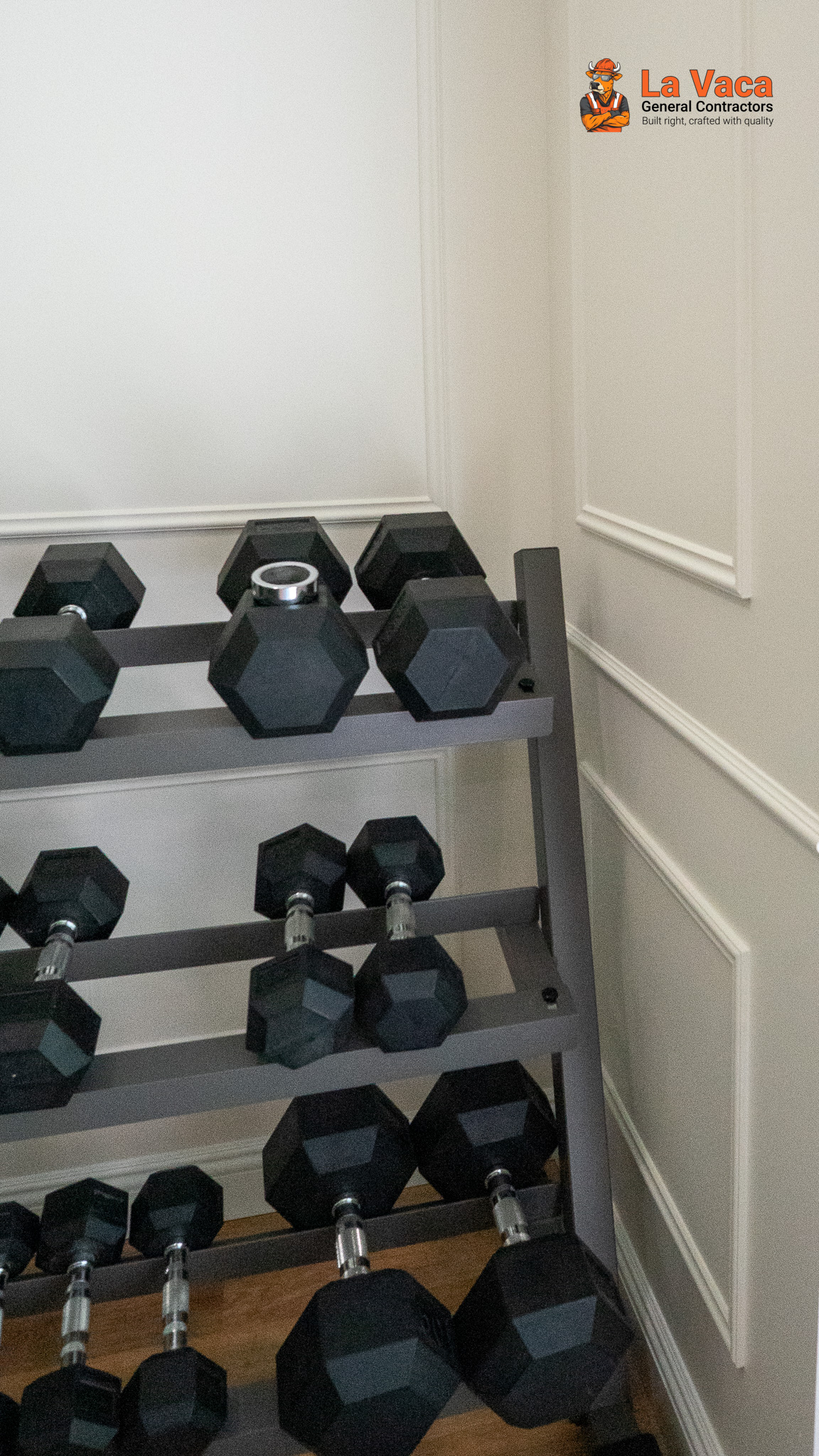 Home gym with black hexagonal dumbbells on metal rack, light gray walls, and white panel molding after Basement Finishing in Kinnelon, NJ