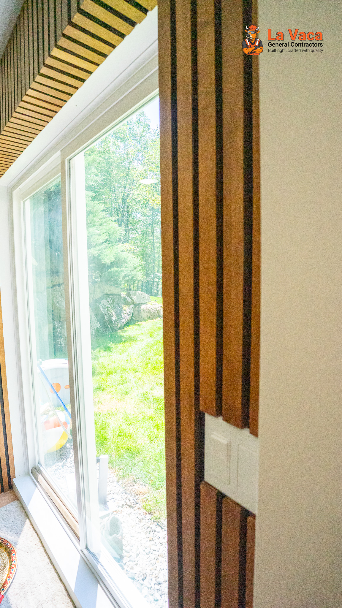 Basement room featuring modern wooden slat wall panels, white trim, and large window overlooking a yard after Basement Finishing in Kinnelon, NJ