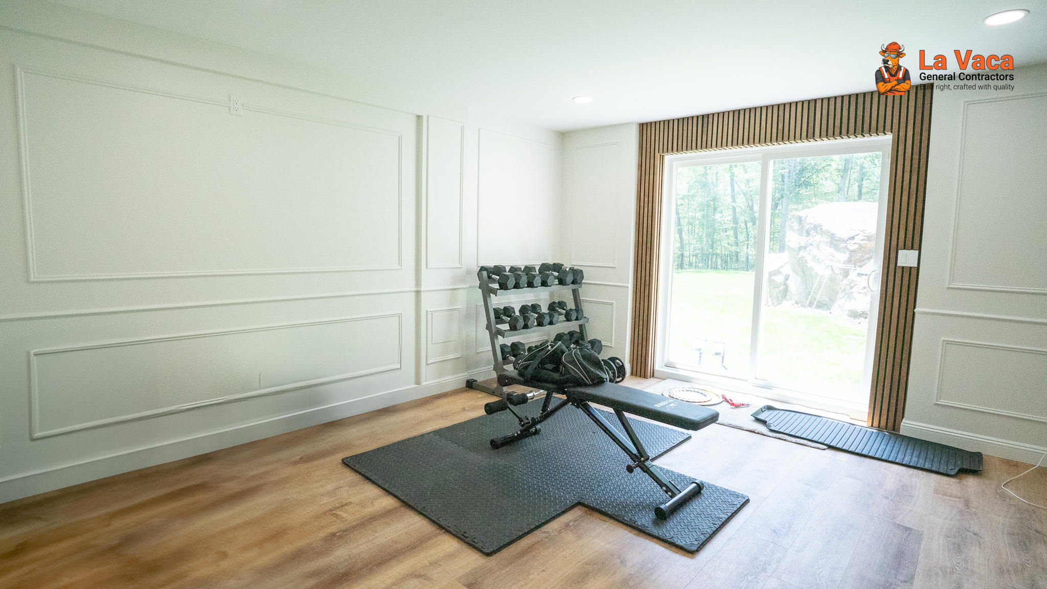 Basement gym with white wainscoting, wood slat accent wall, LVP flooring, and patio door after Basement Finishing in Kinnelon, NJ