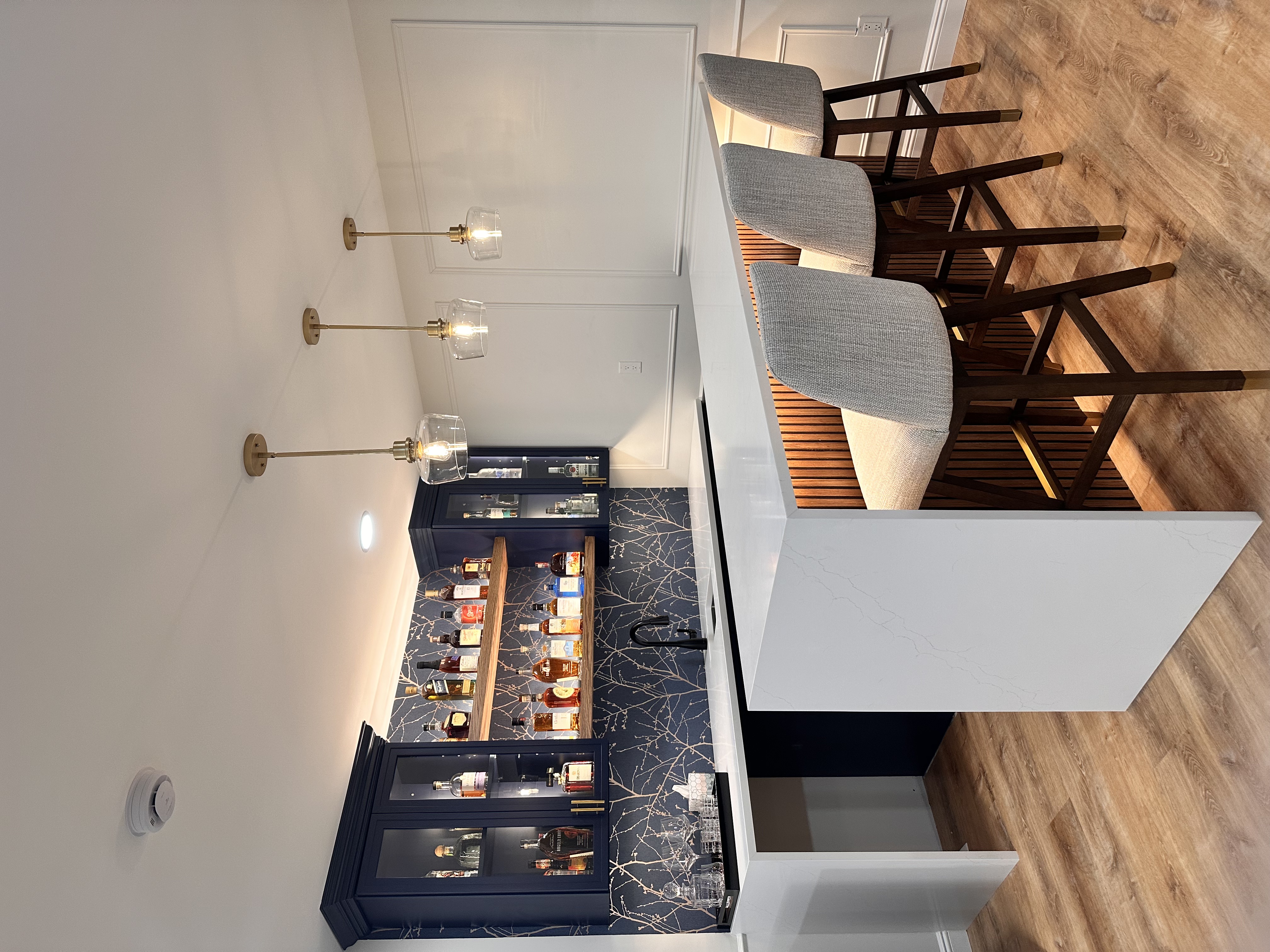 Basement bar featuring white quartz countertops, navy cabinets, and wood flooring after Basement Finishing in Kinnelon, NJ