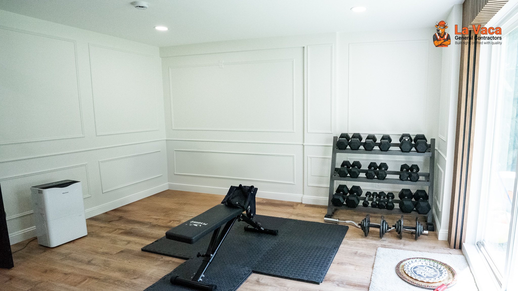Home gym with white paneled walls, wood-look flooring, recessed lighting, and gym equipment after Basement Finishing in Kinnelon, NJ.