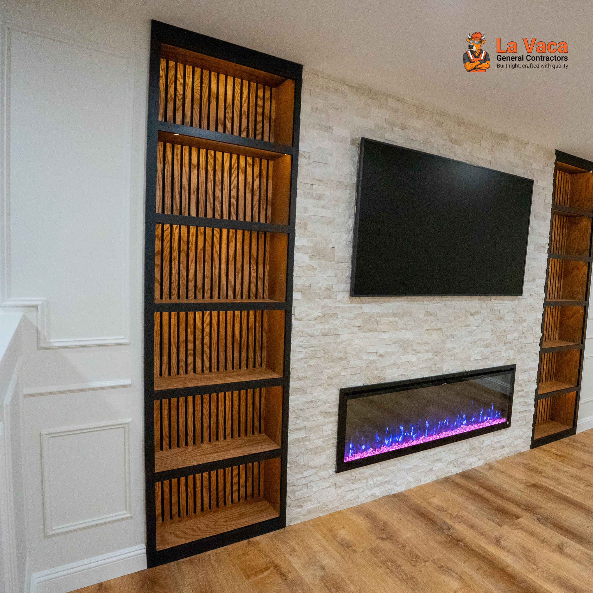 Finished basement living area with built-in dark bookshelves, stone accent wall, purple electric fireplace, TV, and wood-look flooring after Basement Finishing in Kinnelon, NJ