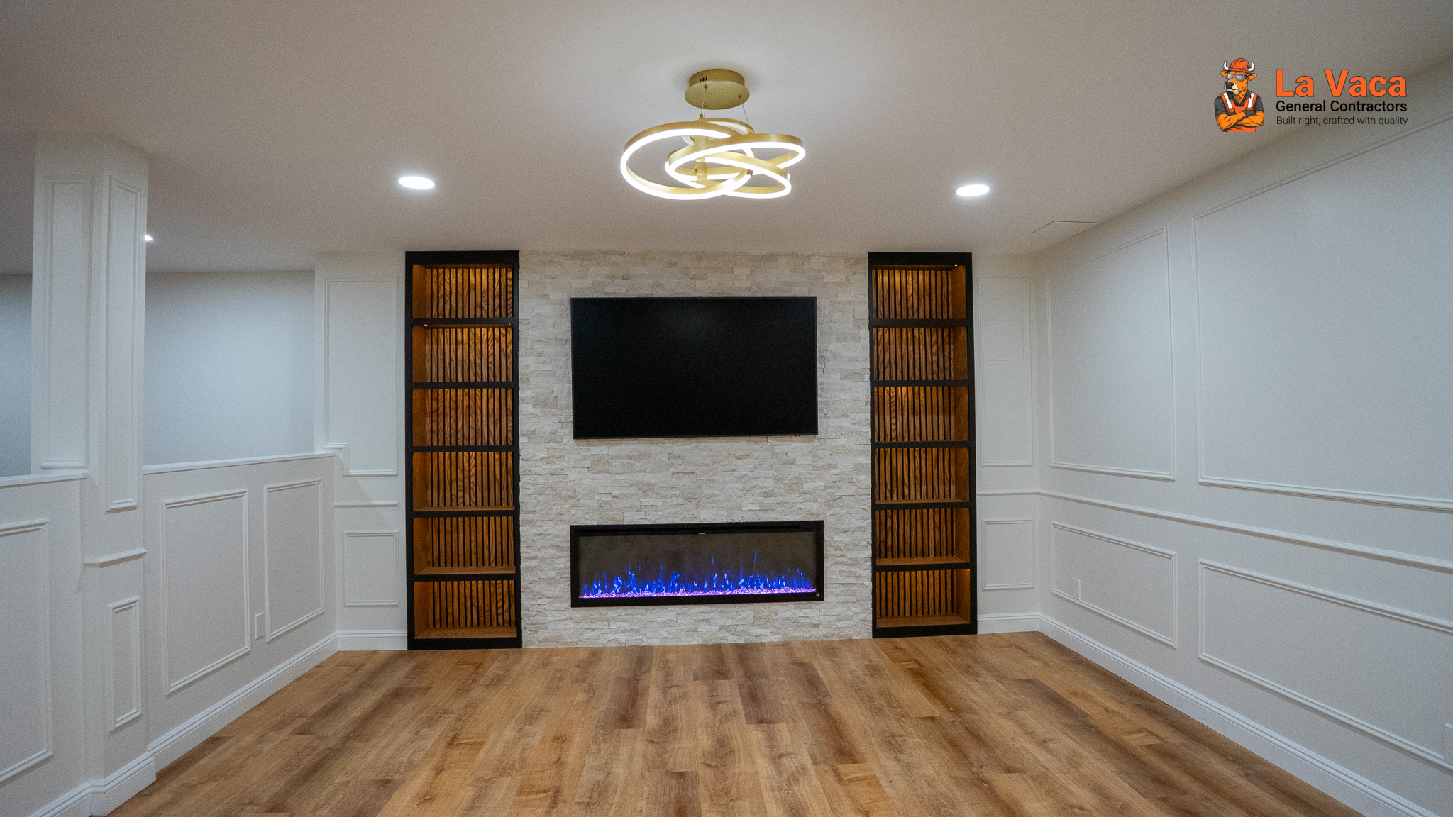 Finished basement living room with faux wood flooring, white wainscoting, integrated TV, electric fireplace, and built-in shelving in Kinnelon, NJ.