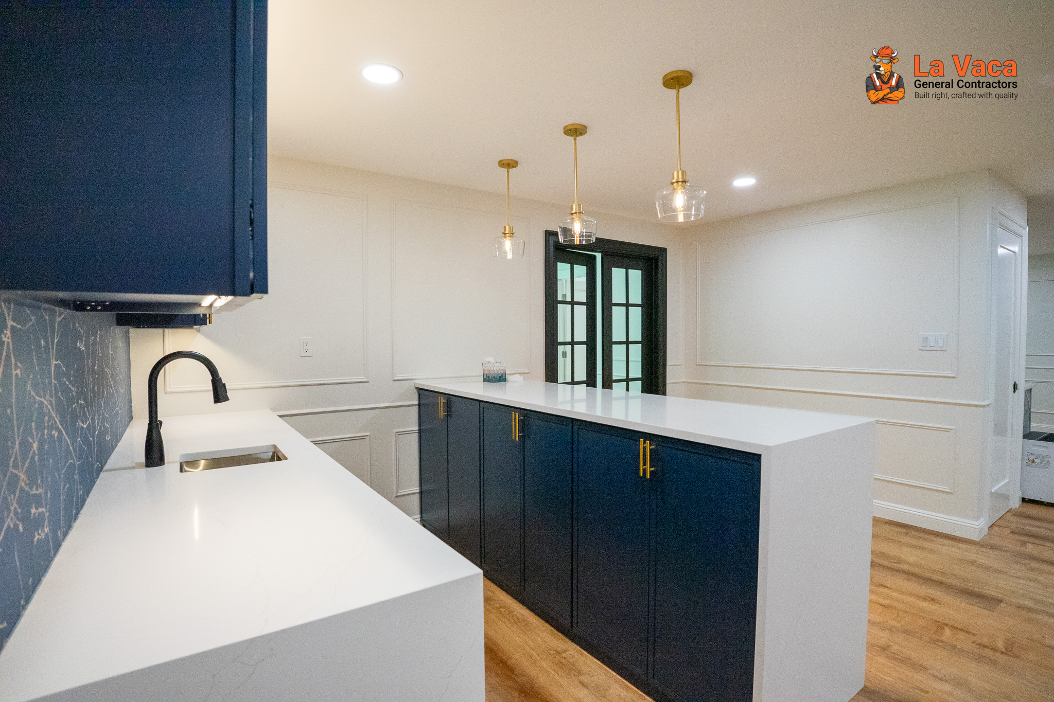 Basement kitchen/bar featuring navy blue cabinetry, white quartz countertops, gold hardware, and wood-look flooring after Basement Finishing in Kinnelon, NJ