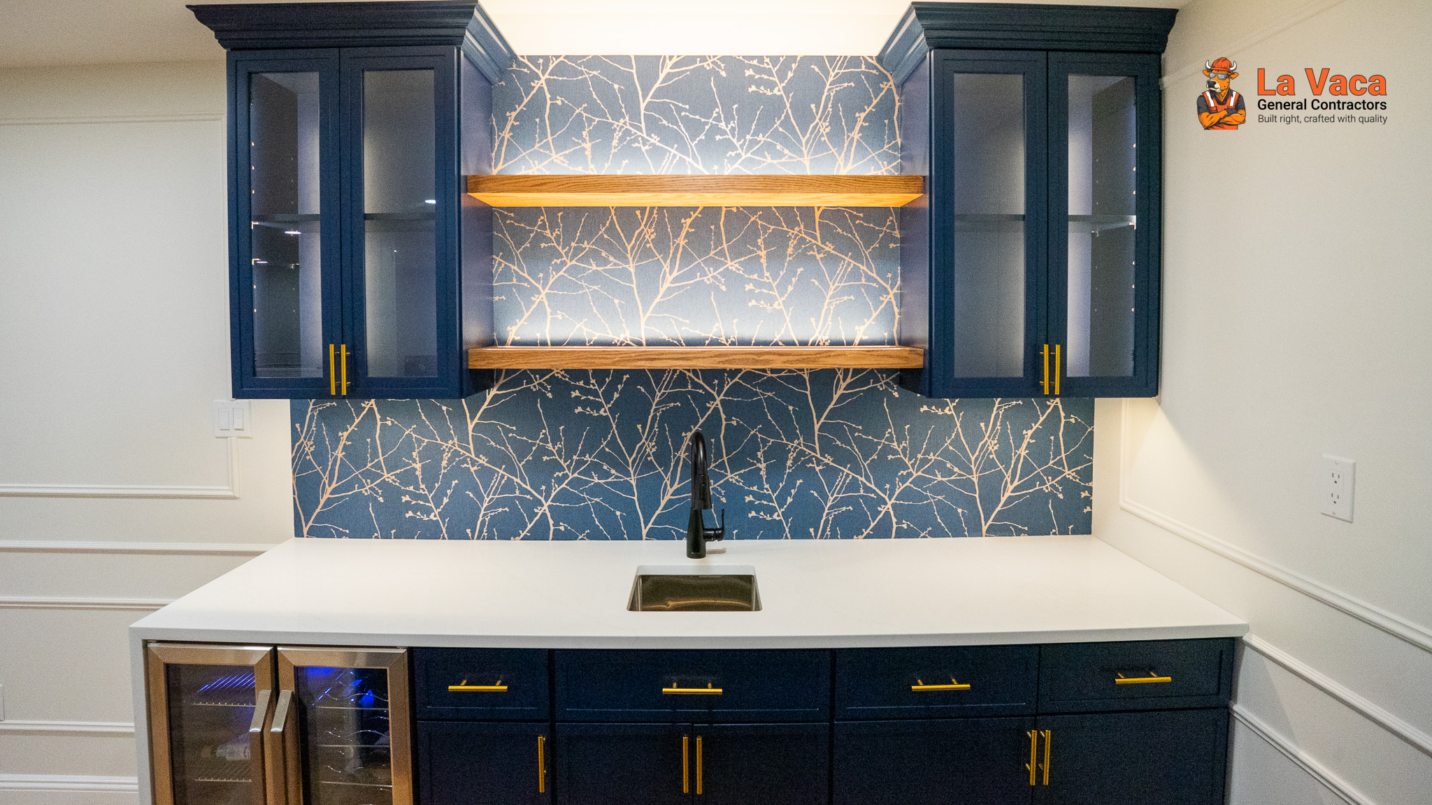 Wet bar featuring blue cabinetry, white quartz countertops, and tree-patterned wallpaper after Basement Finishing in Kinnelon, NJ.