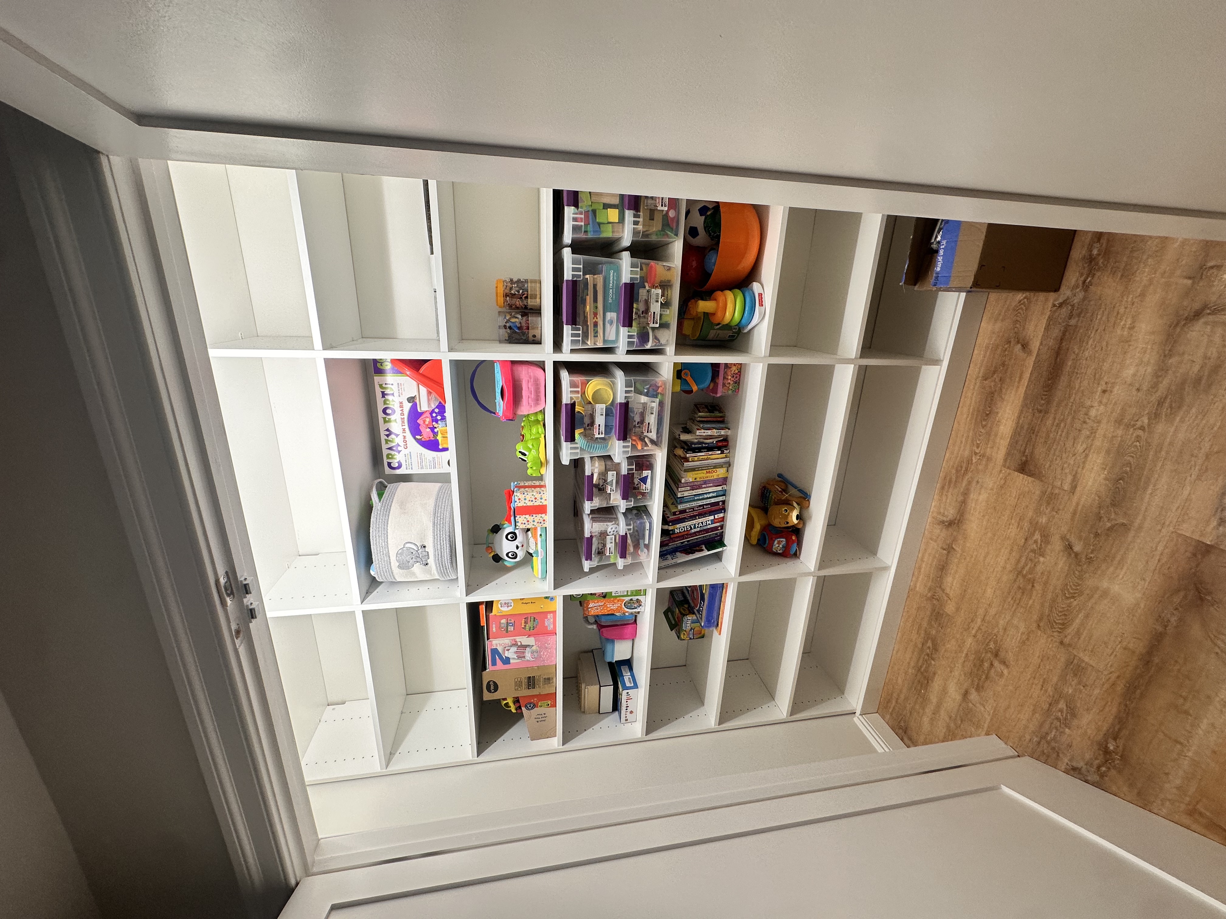 Finished basement storage closet featuring white built-in shelves/doors, light wood-look flooring after Basement Finishing in Kinnelon, NJ.