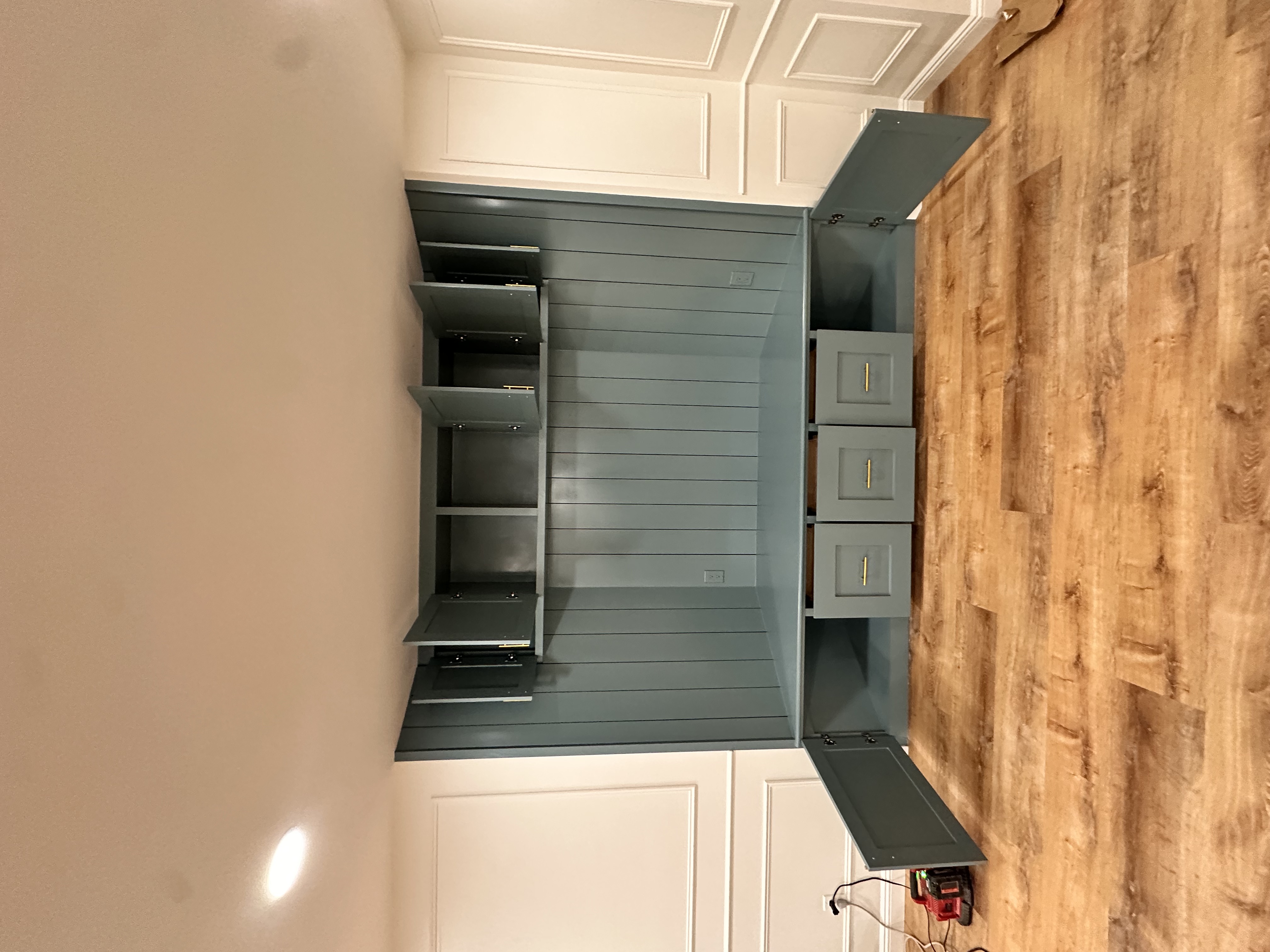 Basement living area featuring a custom teal built-in with storage and wood-look laminate flooring after Basement Finishing in Kinnelon, NJ.