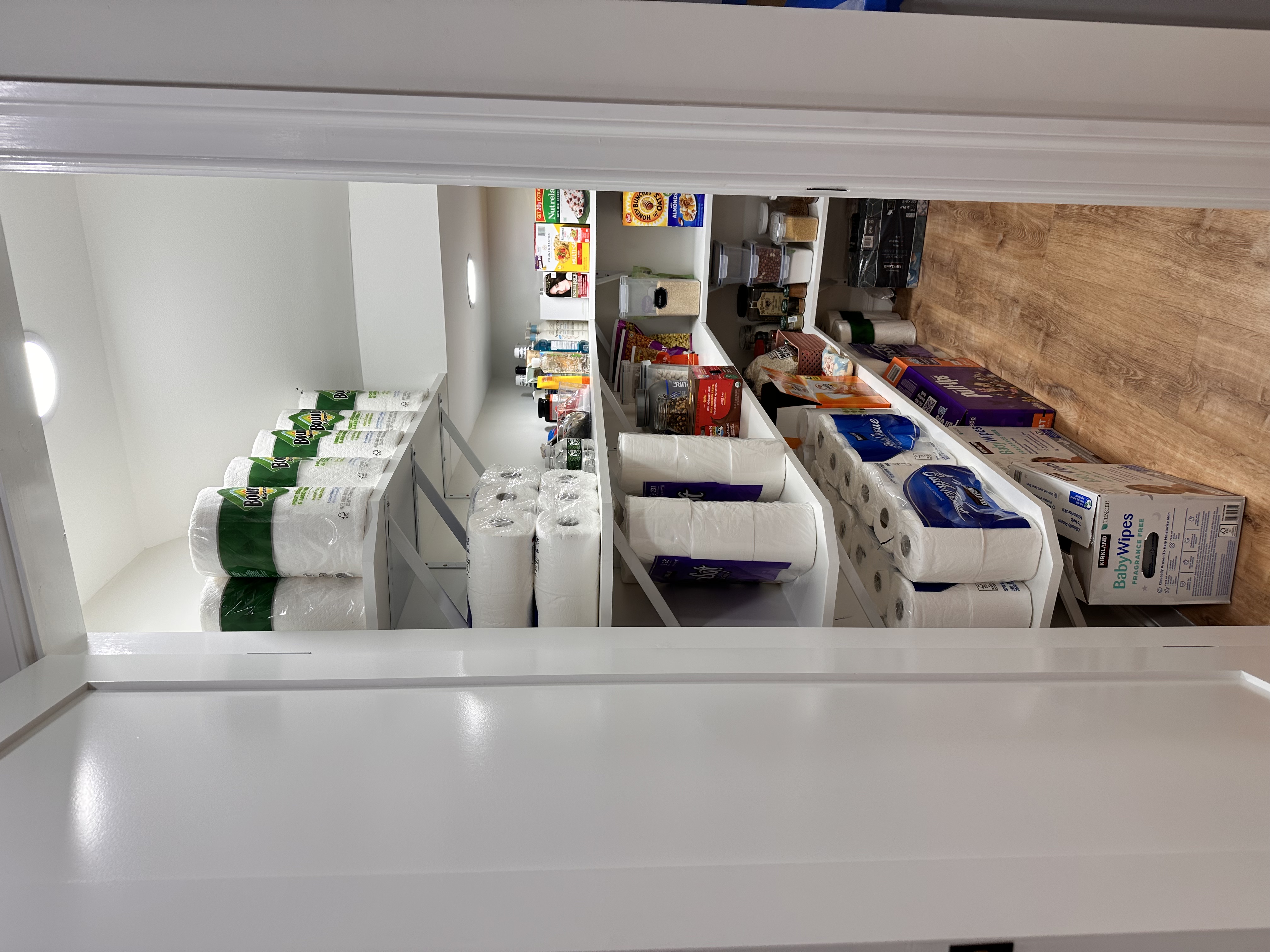 Pantry with white shelves, recessed lighting, and wood-look flooring after Basement Finishing in Kinnelon, NJ.